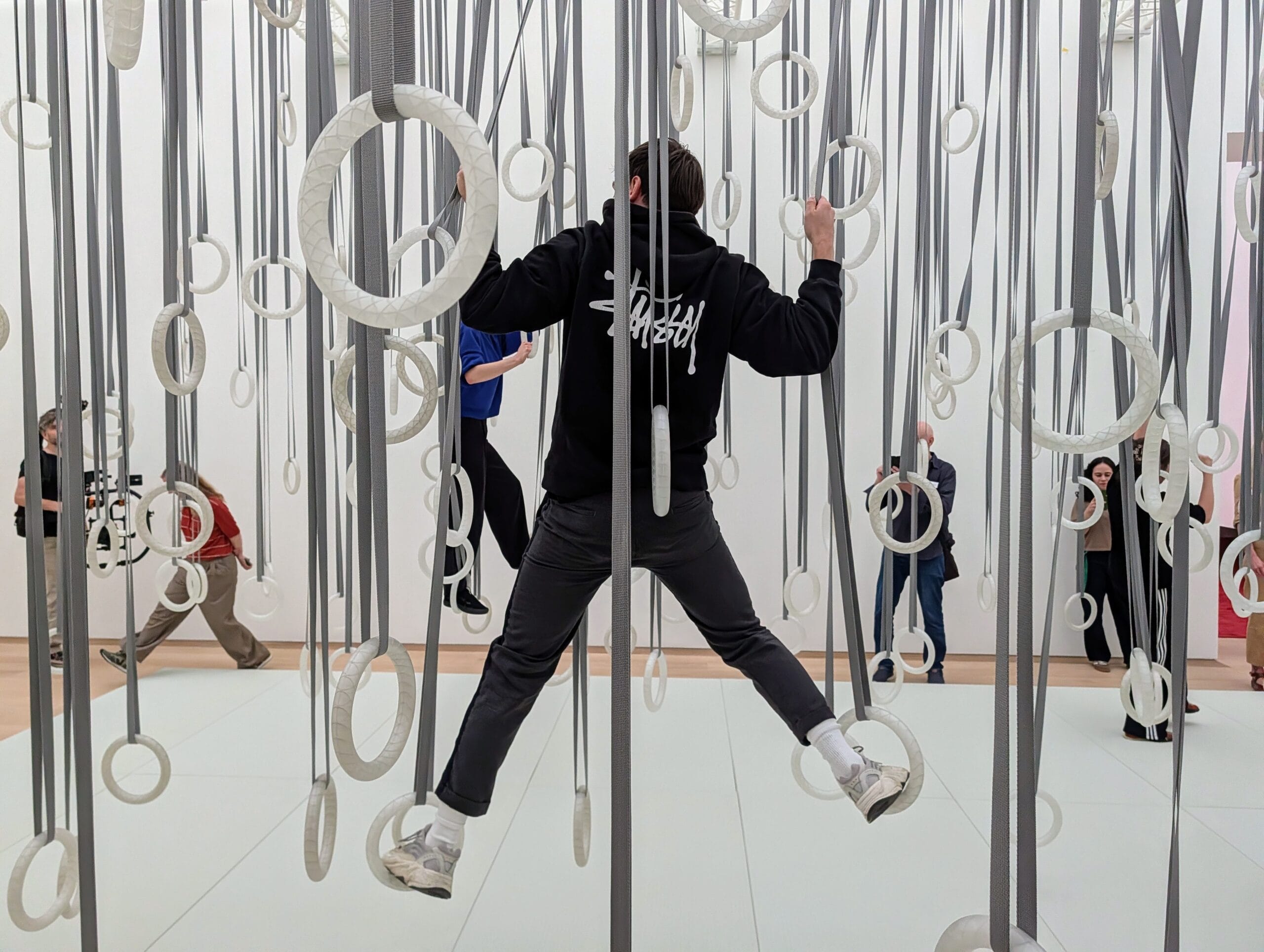Een persoon klimt in een interactieve kunstinstallatie bestaande uit tientallen witte ringen die aan grijze banden hangen