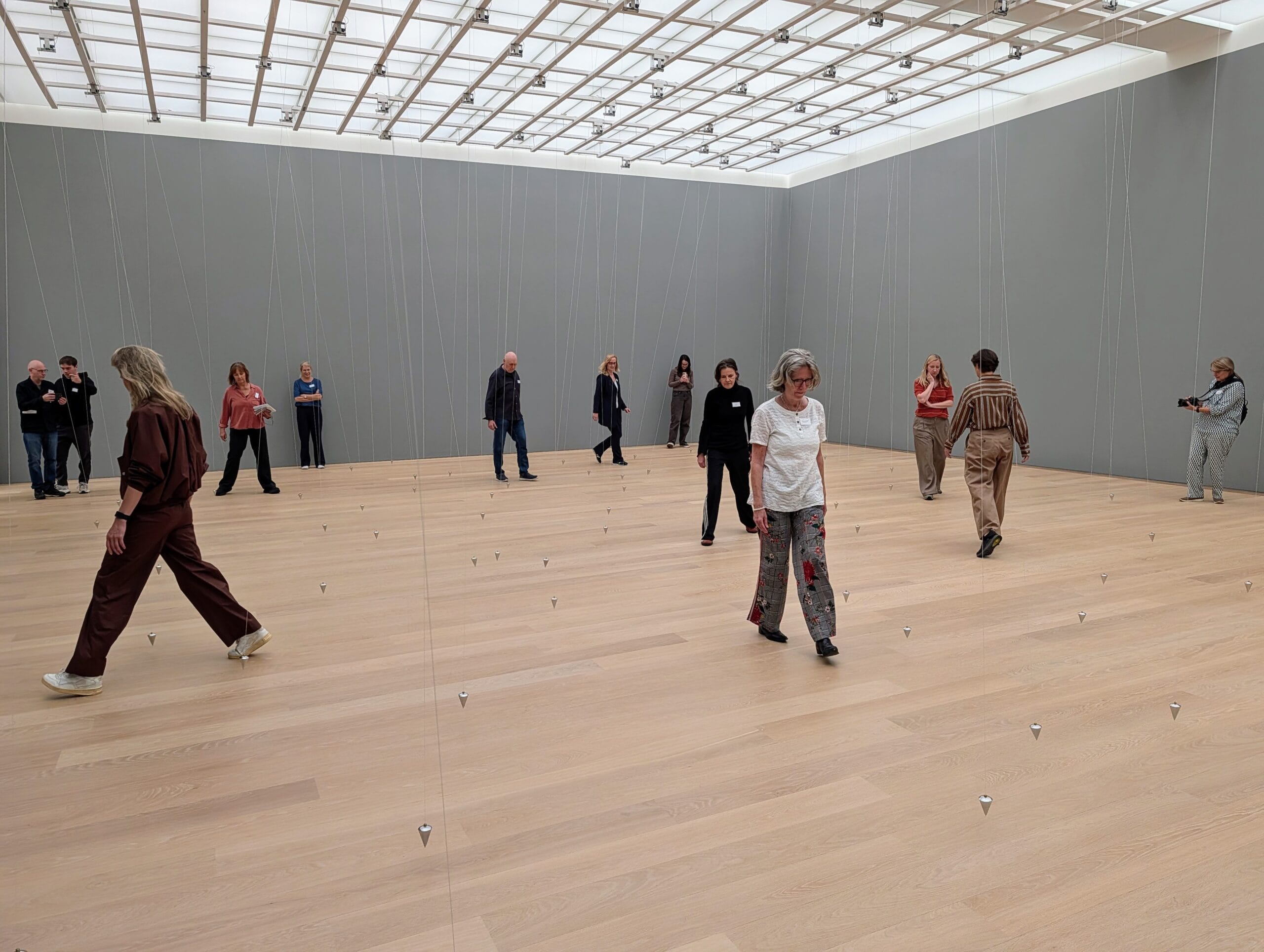 Bezoekers wandelen door een kunstinstallatie met honderden zilveren pendels die aan dunne draden in een grote zaal hangen