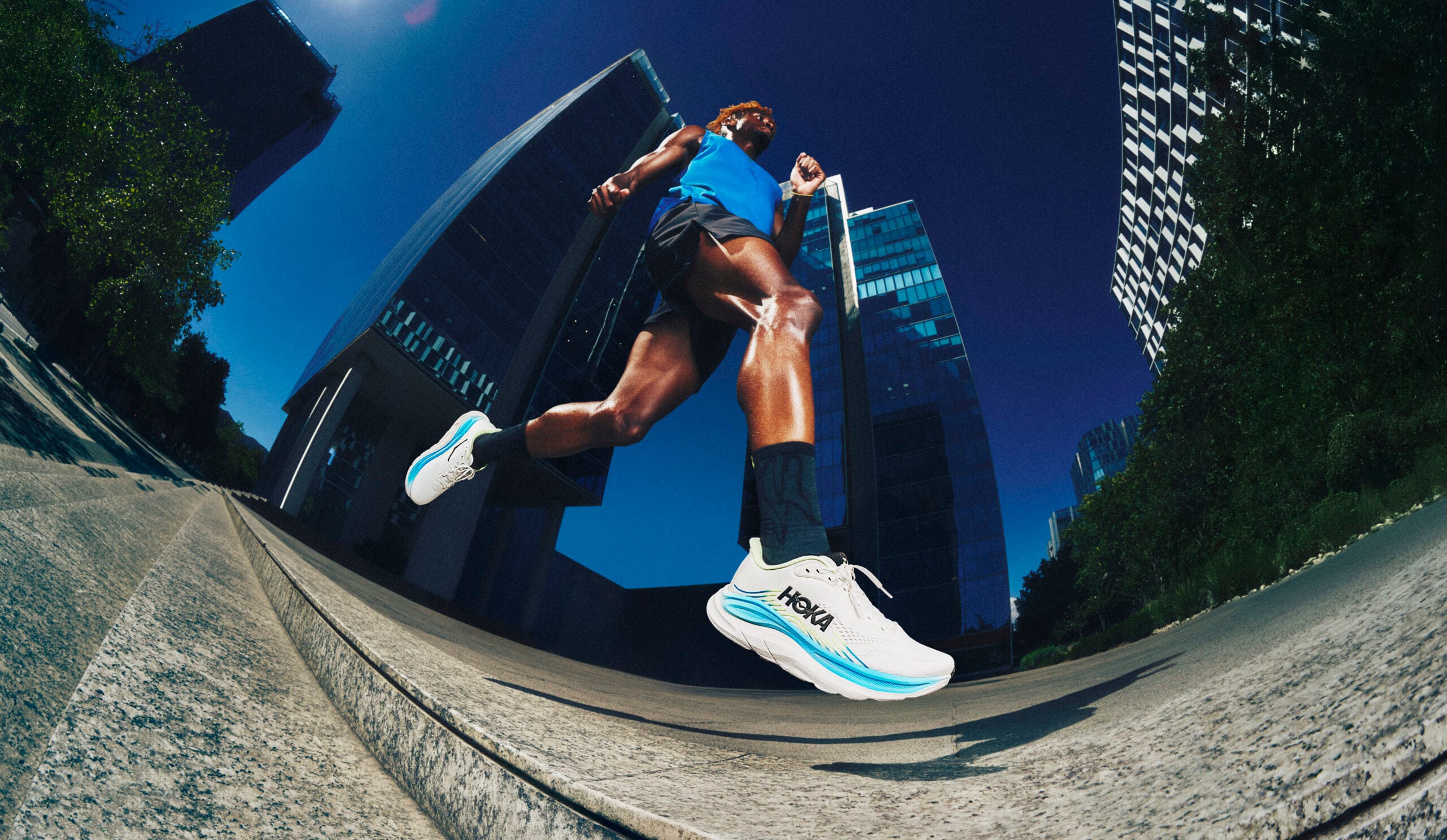 Hardloper in actie door een stad met moderne wolkenkrabbers, dragend Hoka hardloopschoenen model Clifton 11