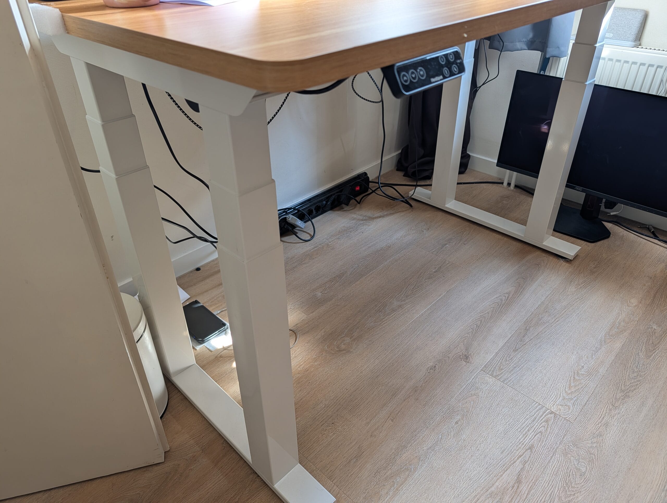 In hoogte verstelbaar bureau met een houten blad, wit onderstel en een bedieningspaneel aan de voorzijde