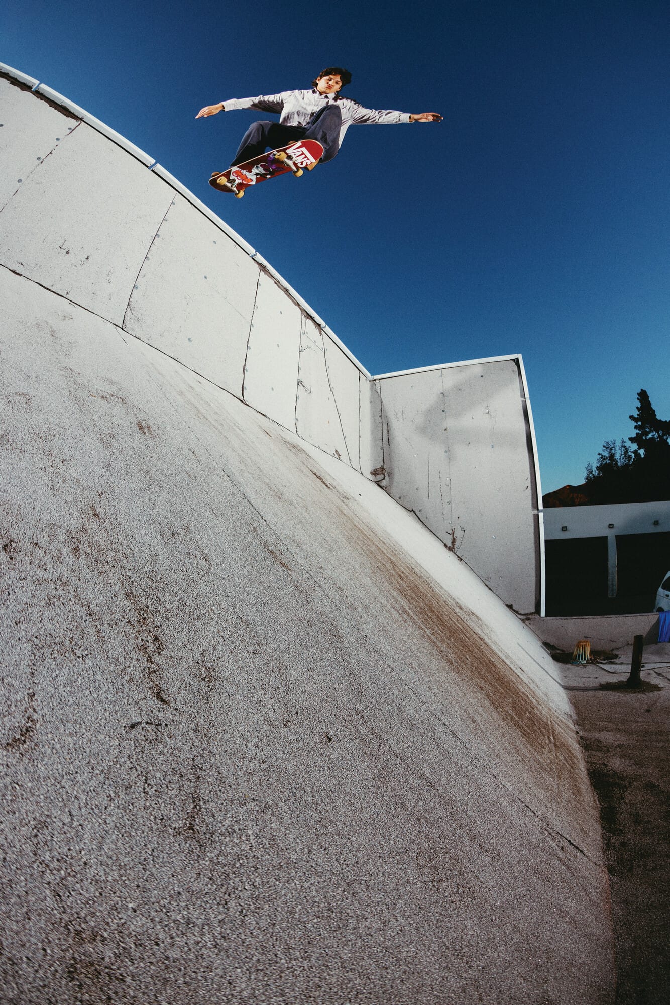 Een skateboarder maakt een sprong in de lucht boven een betonnen helling tegen een strakblauwe lucht