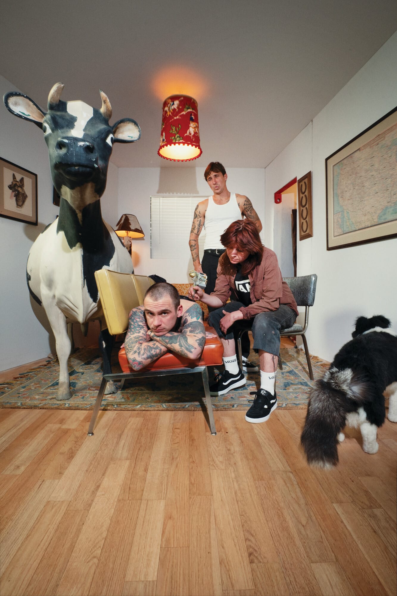 Een vrouw zet een tatoeage op de rug van een man in een kamer met een groot koeienbeeld en een hond
