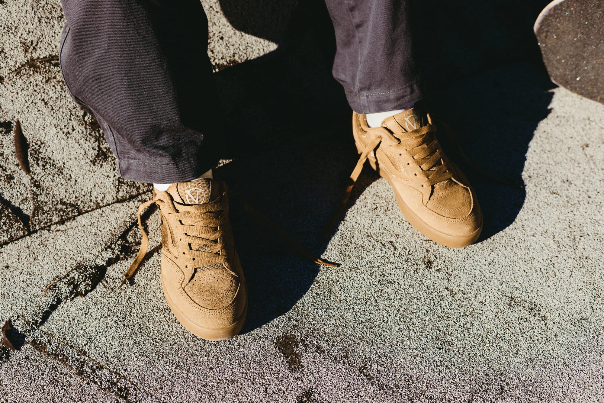 Close-up van een persoon die bruine suède Vans skateschoenen draagt op een ruwe ondergrond