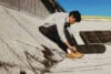 Een jonge man zit op een betonnen helling en strikt de veters van zijn bruine sneakers naast zijn skateboard