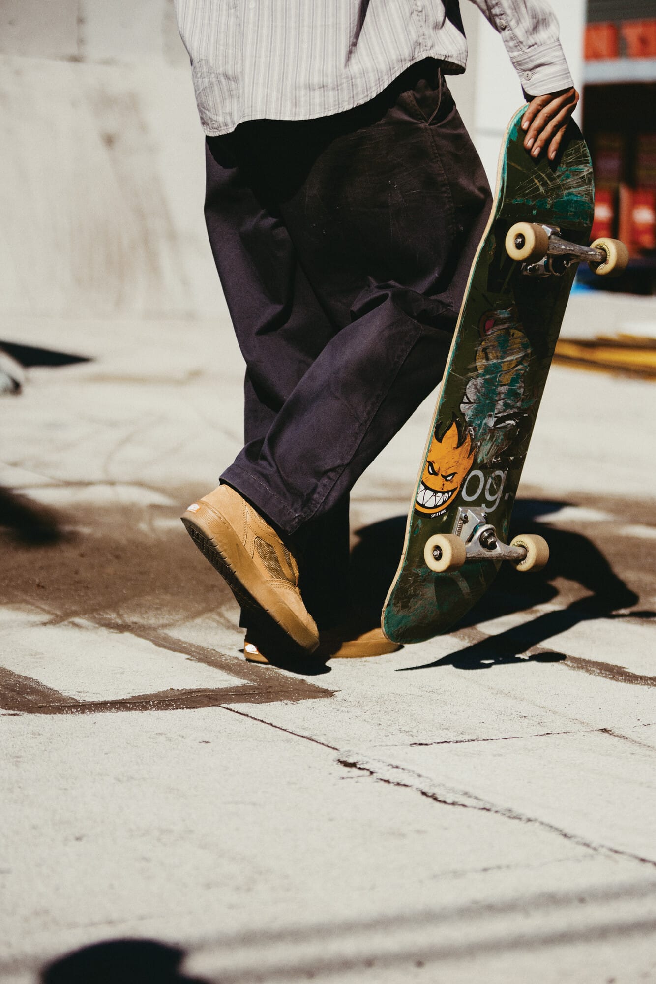 Een skateboarder van achteren gezien die een versleten skateboard vasthoudt terwijl hij op een betonnen ondergrond staat
