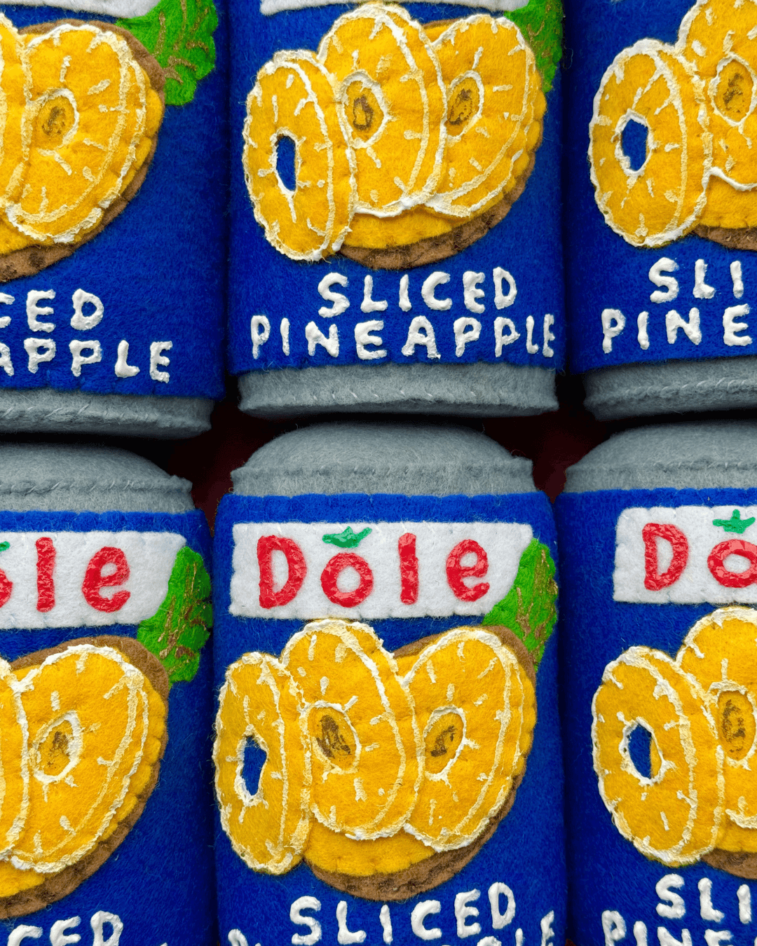 Close-up van handgemaakte vilten conservenblikken van Dole Sliced Pineapple met geborduurde details
