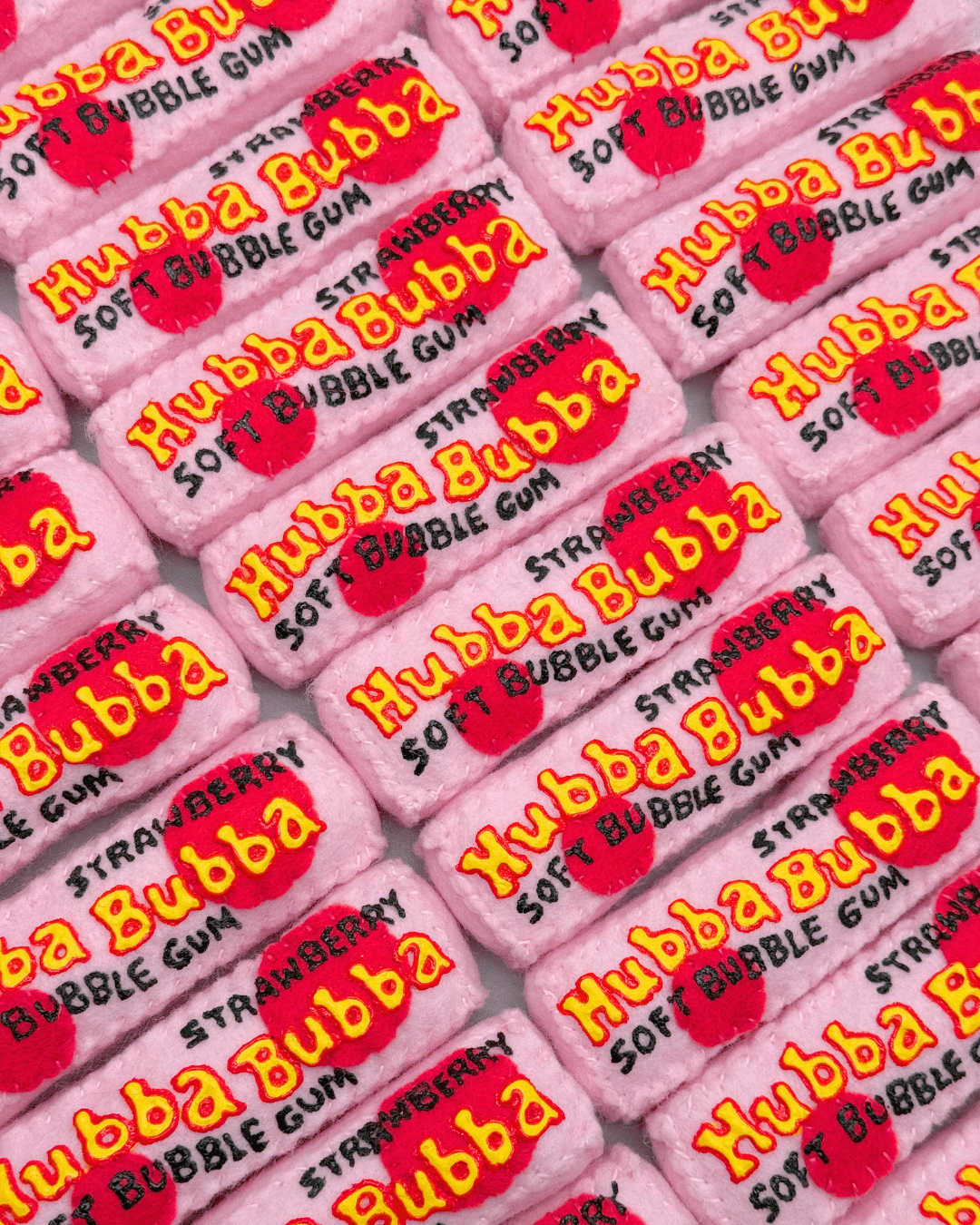 Een verzameling handgemaakte vilten pakjes Hubba Bubba kauwgom in de smaak aardbei, met geborduurde logo's en details