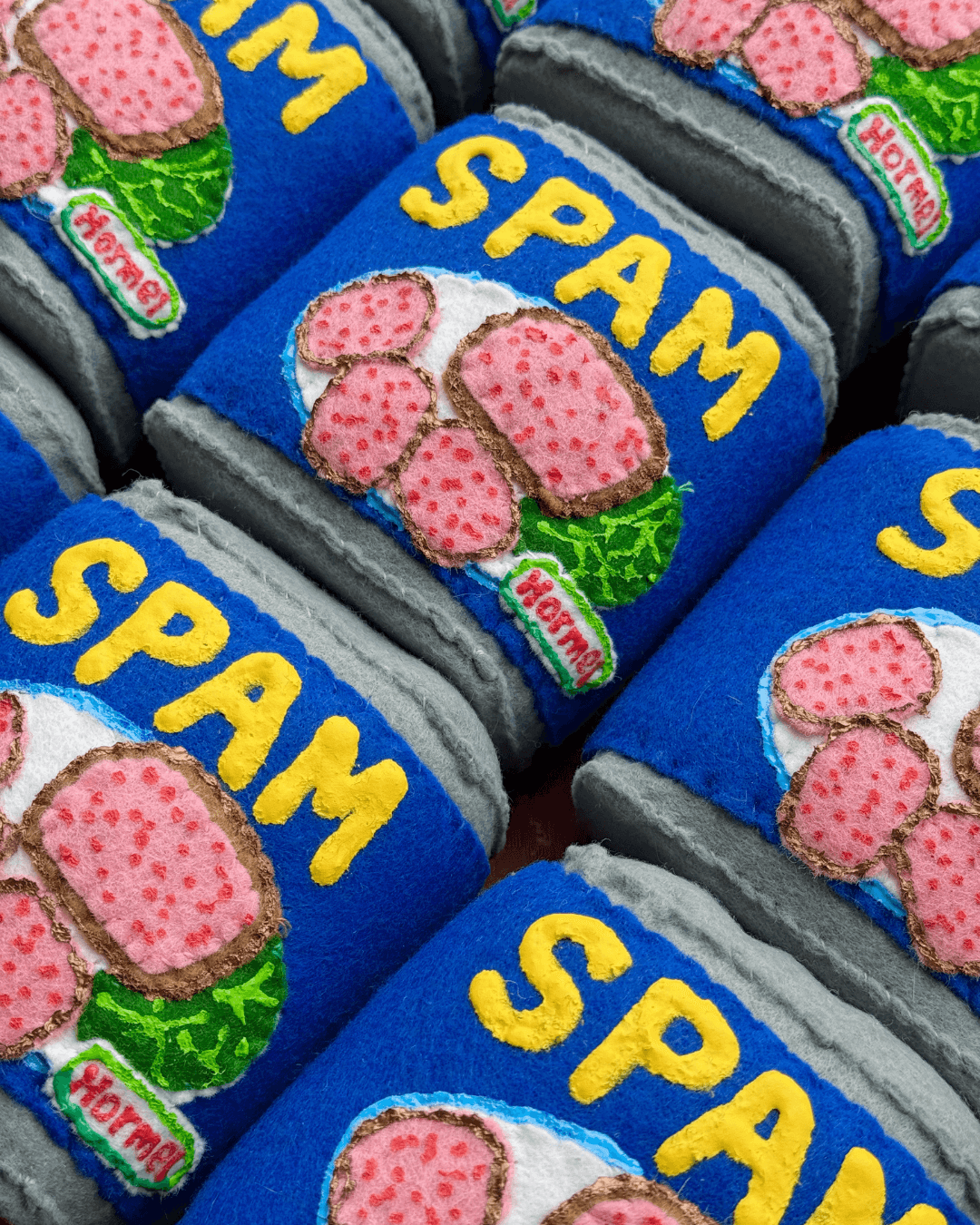 Verschillende handgemaakte vilten blikjes Spam met geborduurde details en gele letters op een blauwe achtergrond