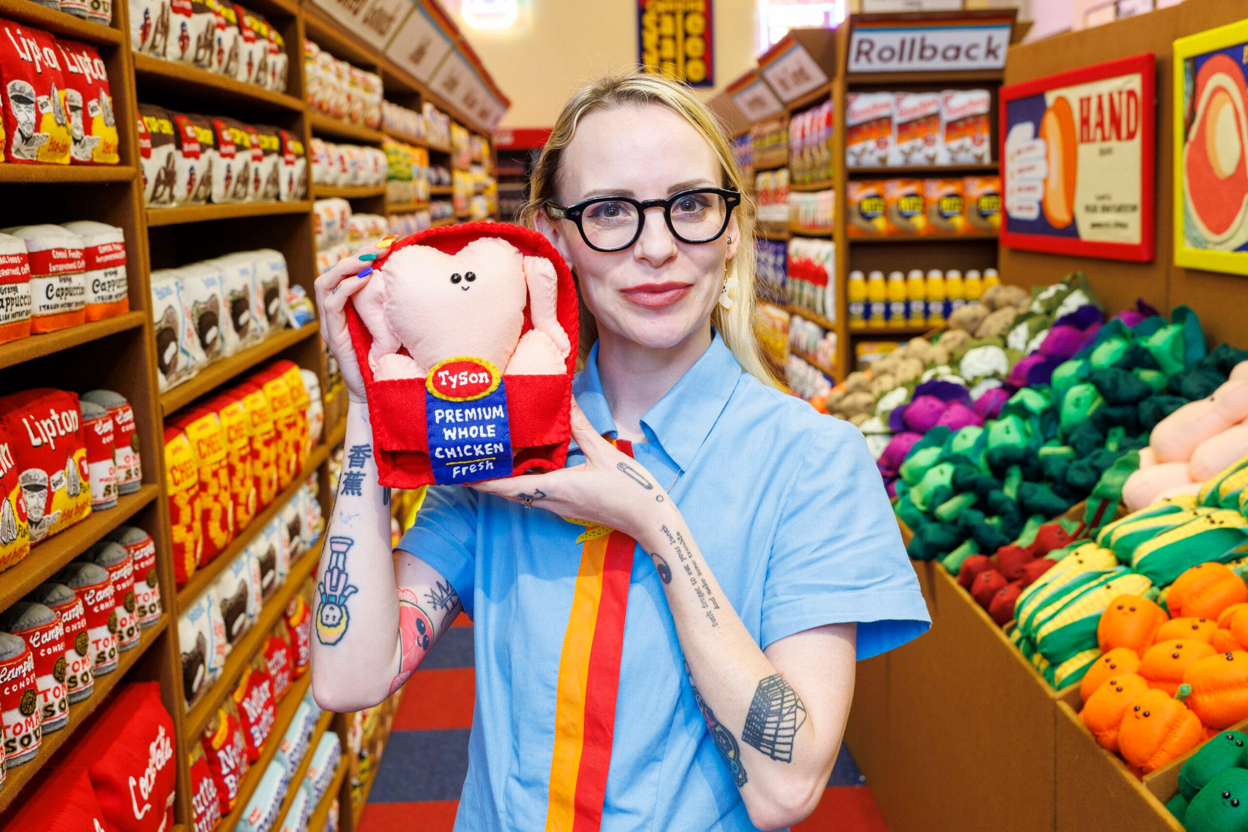 Kunstenaar Lucy Sparrow in haar vilten supermarkt, terwijl ze een handgemaakte kip van vilt vasthoudt