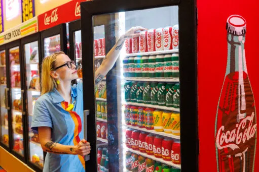 Een vrouw pakt een frisdrankblikje van vilt uit een koeling in een supermarkt die volledig uit viltkunst bestaat