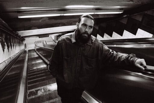 Een bebaarde man in een spijkerjasje staat op een roltrap in een metrostation