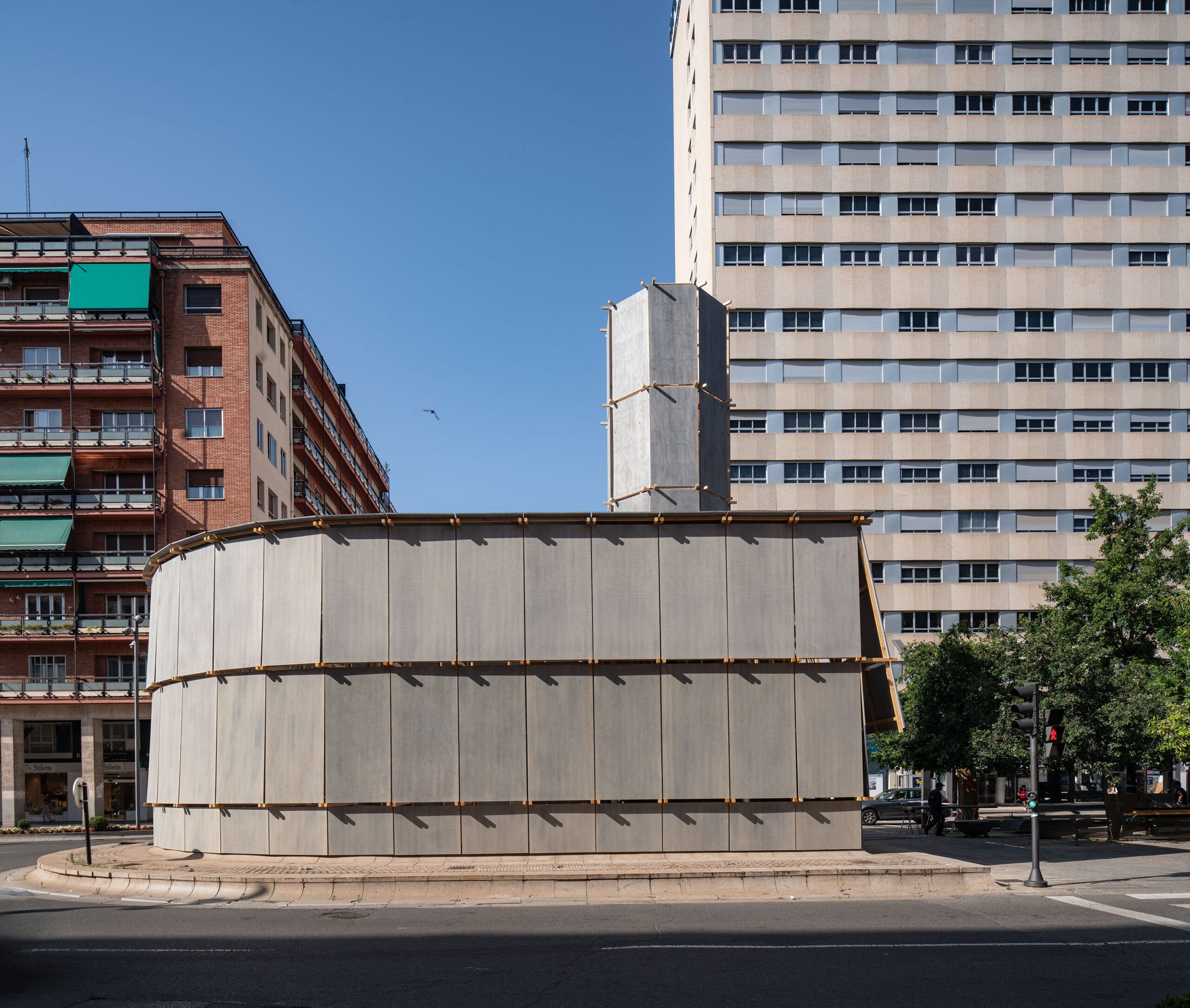De houten installatie Round About Baths op een rotonde in Logroño, bestaande uit hoge grijze wanden en een centrale toren