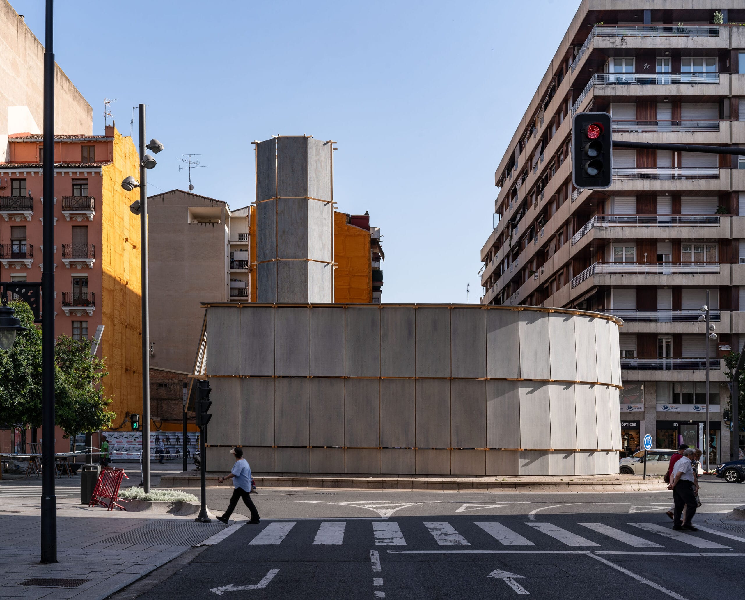 De houten installatie Round About Baths op een rotonde in Logroño, omringd door stadsgebouwen en een zebrapad
