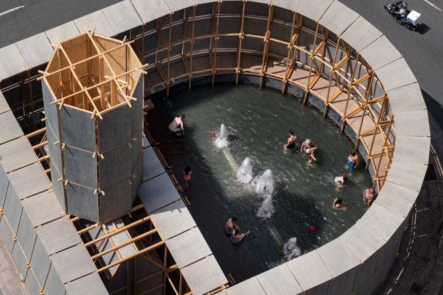 Bovenaanzicht van mensen die zwemmen in een tijdelijk houten zwembad met fonteinen op een stadsplein