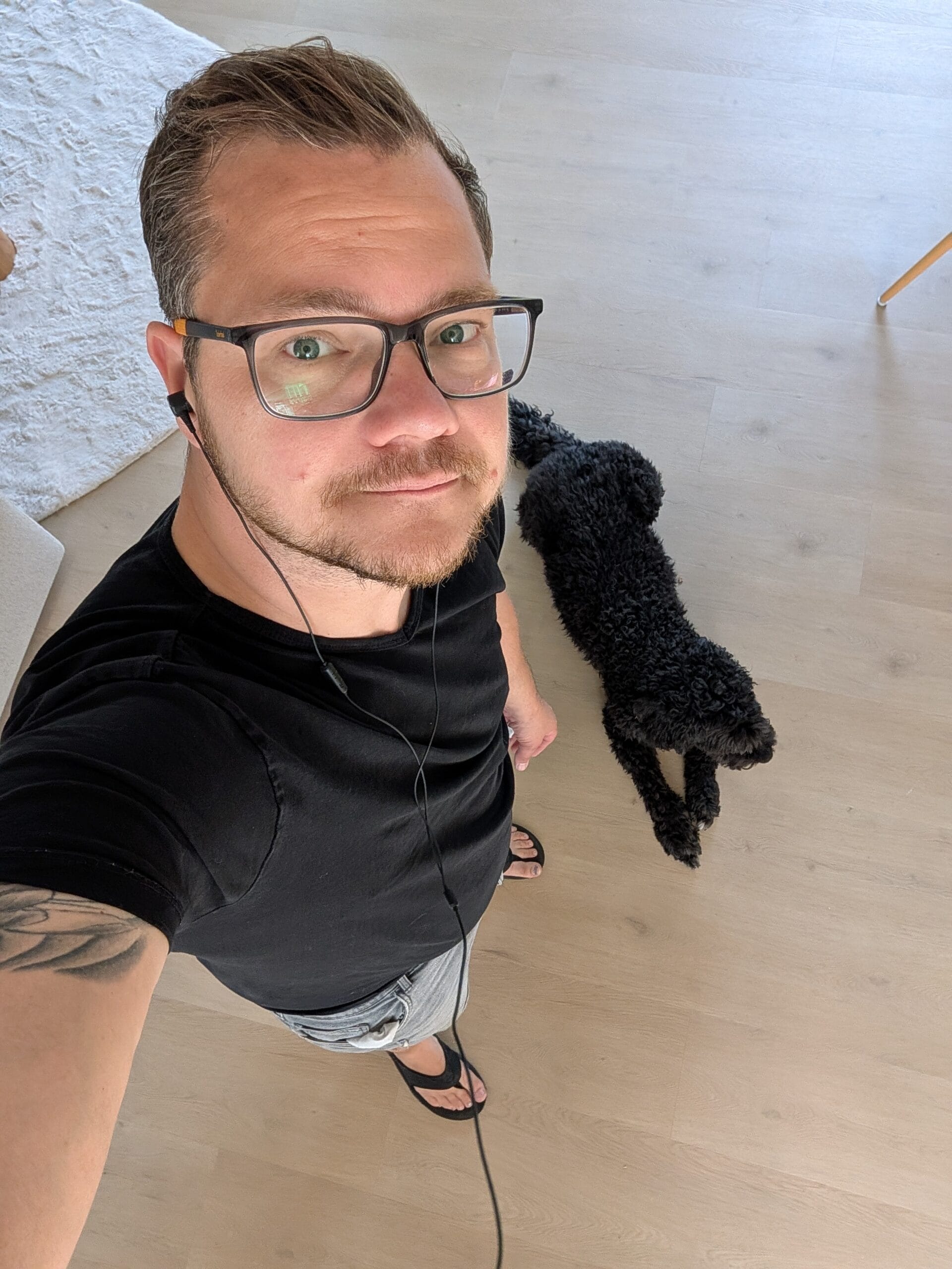 Sander Noordijk draagt de bedrade Teufel Move 2 oordopjes terwijl hij in een woonkamer staat met een zwarte hond