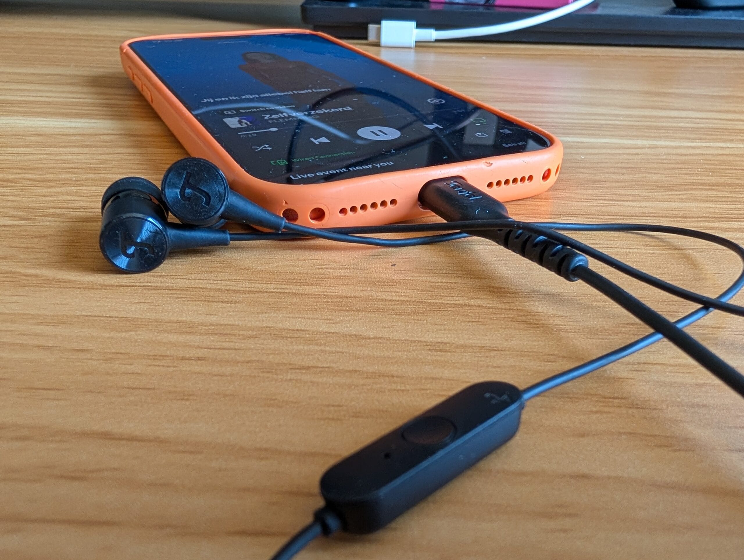De zwarte Teufel Move 2 oordopjes aangesloten via de USB-C poort van een smartphone in een oranje hoesje