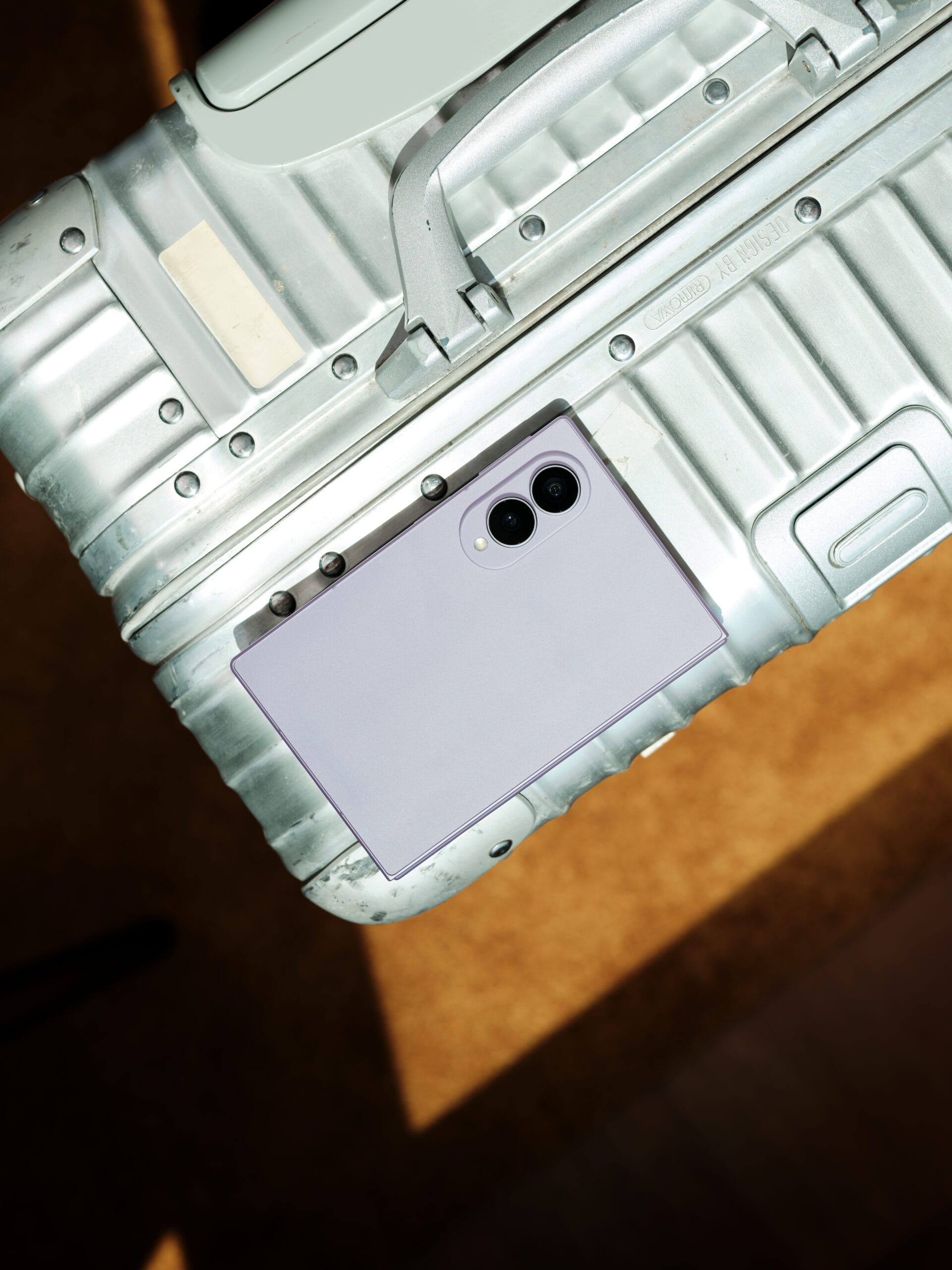 Bovenaanzicht van een dichtgeklapte, lichtpaarse Samsung Galaxy Z Flip8 op een zilverkleurige koffer