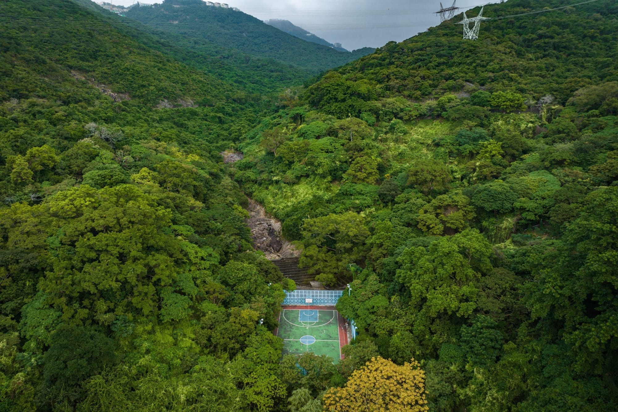 Luchtfoto van een groen basketbalveld verscholen in een dichtbegroeide, beboste vallei in Hong Kong