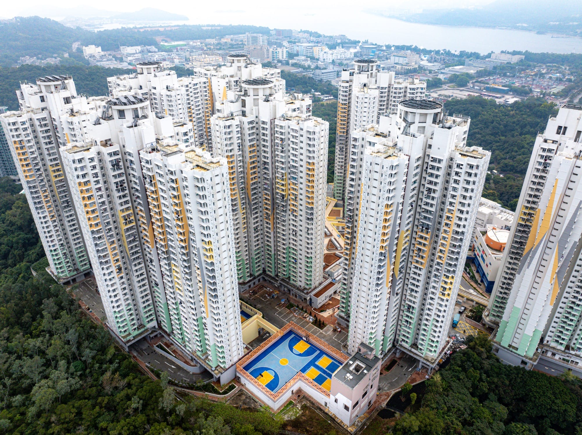 Luchtfoto van een blauw-geel basketbalveld tussen torenhoge witte wolkenkrabbers in Hong Kong