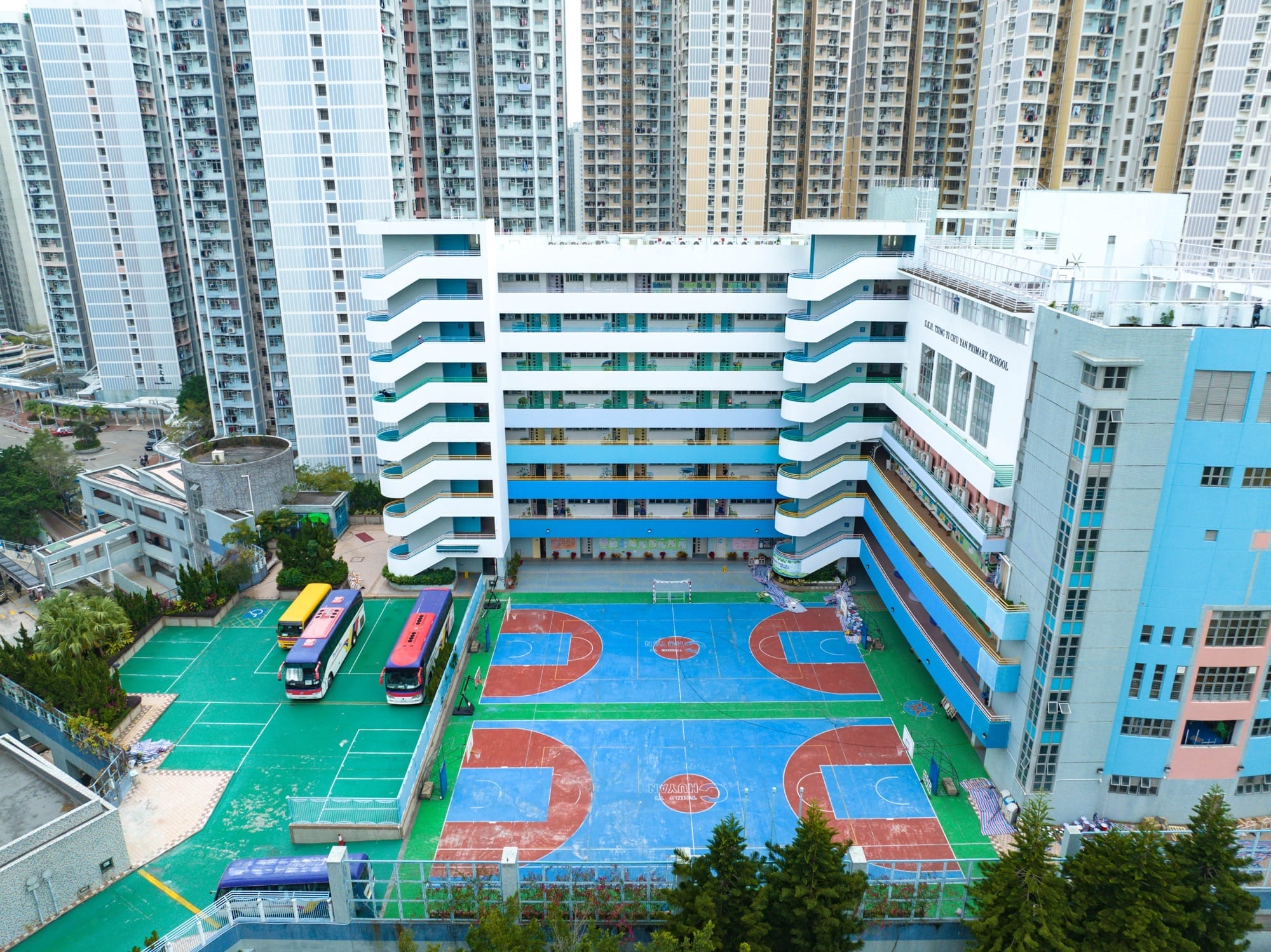 Luchtfoto van een blauw-rood basketbalveld bij een basisschool in Hong Kong, omringd door hoge woontorens