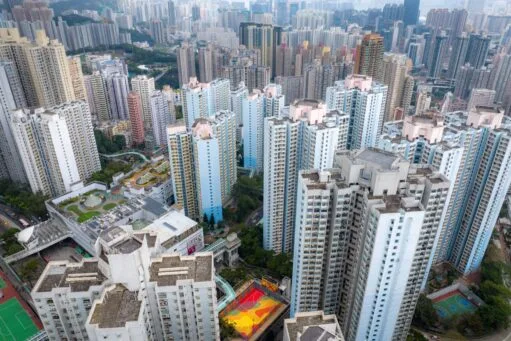 Luchtfoto van een dichtbebouwde wijk in Hong Kong met hoge, lichtblauwe en witte woontorens en een kleurrijk sportveld