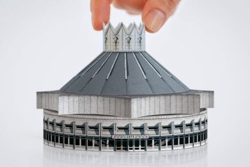 Een hand plaatst de kroon op een miniatuur papieren model van het brutalistische circusgebouw in Chisinau
