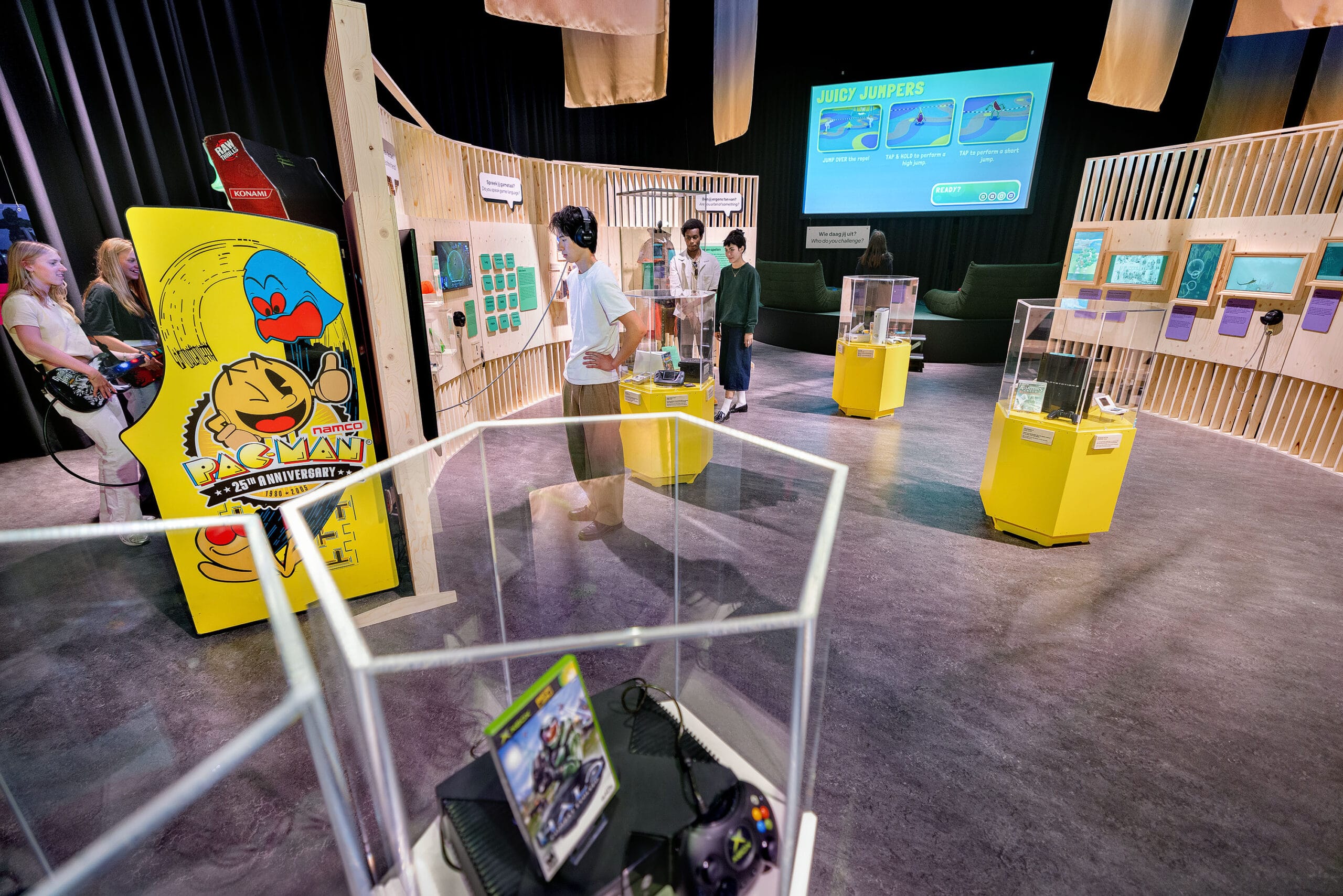 Bezoekers in een interactieve tentoonstelling over de geschiedenis van videogames met vitrines en arcadekasten