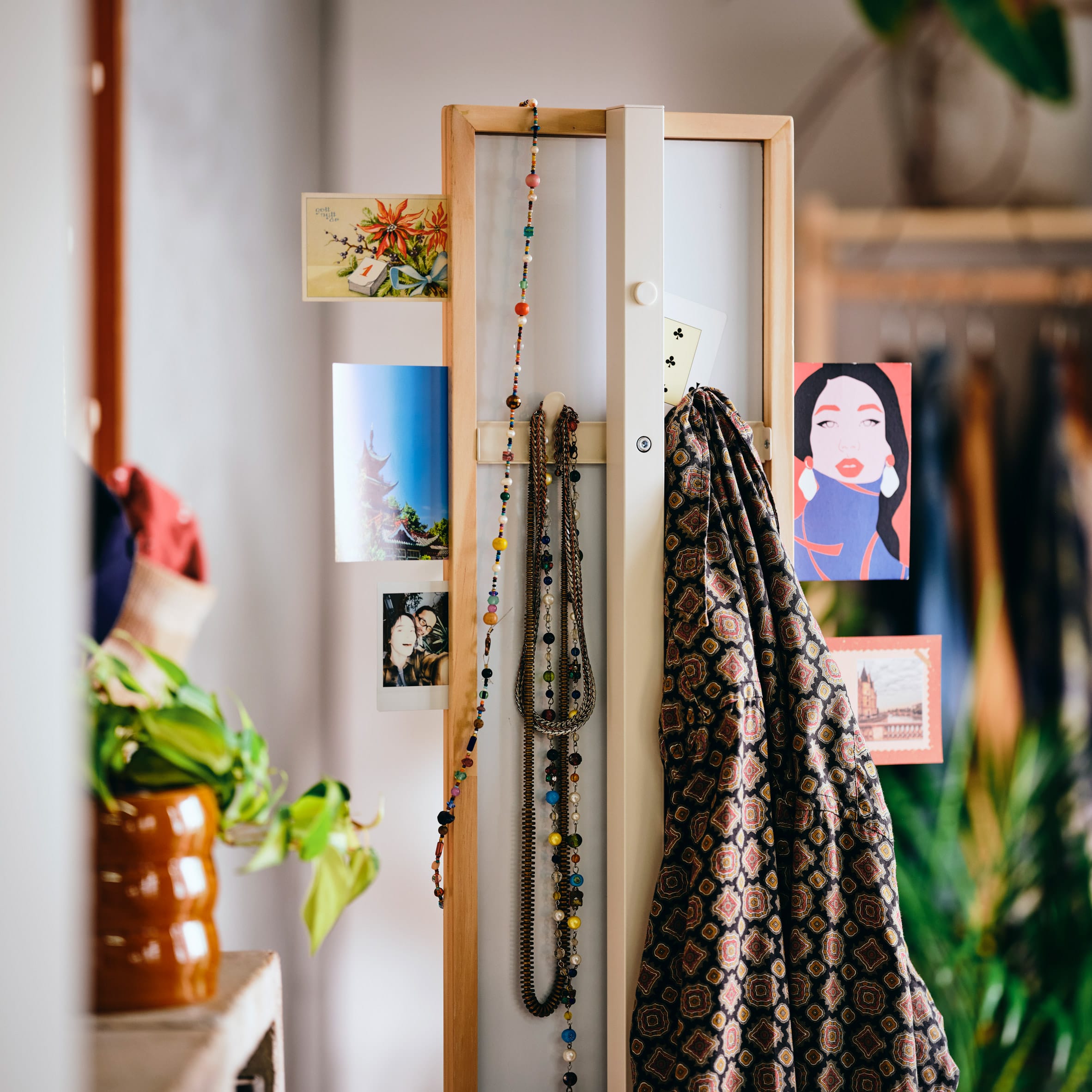 Een smalle, houten organizer uit de KOMPISHÄNG-collectie met daaraan foto's, kettingen en een kledingstuk