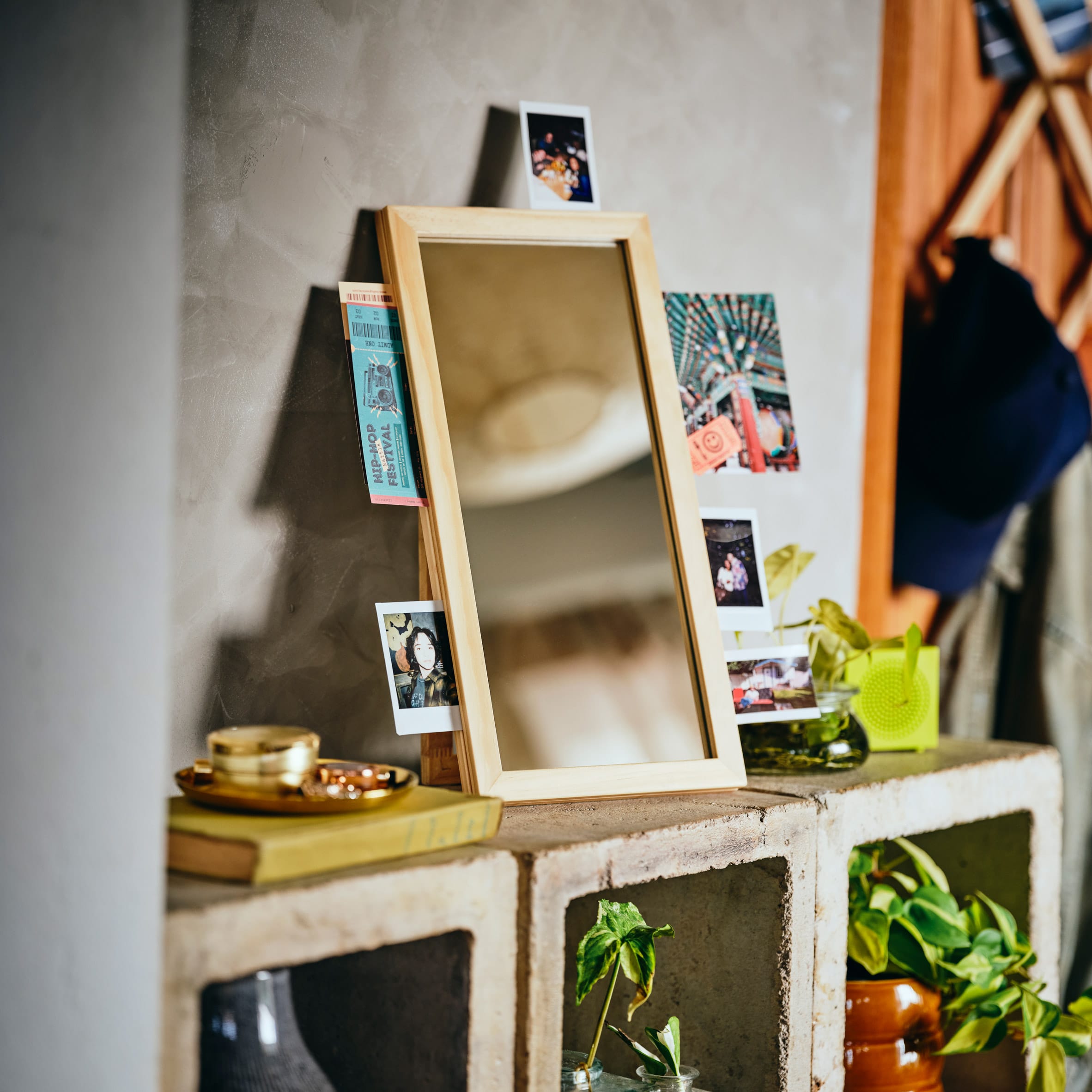Een rechtopstaande spiegel met houten lijst waar foto's en kaartjes achter zijn gestoken, geplaatst op een betonnen kast