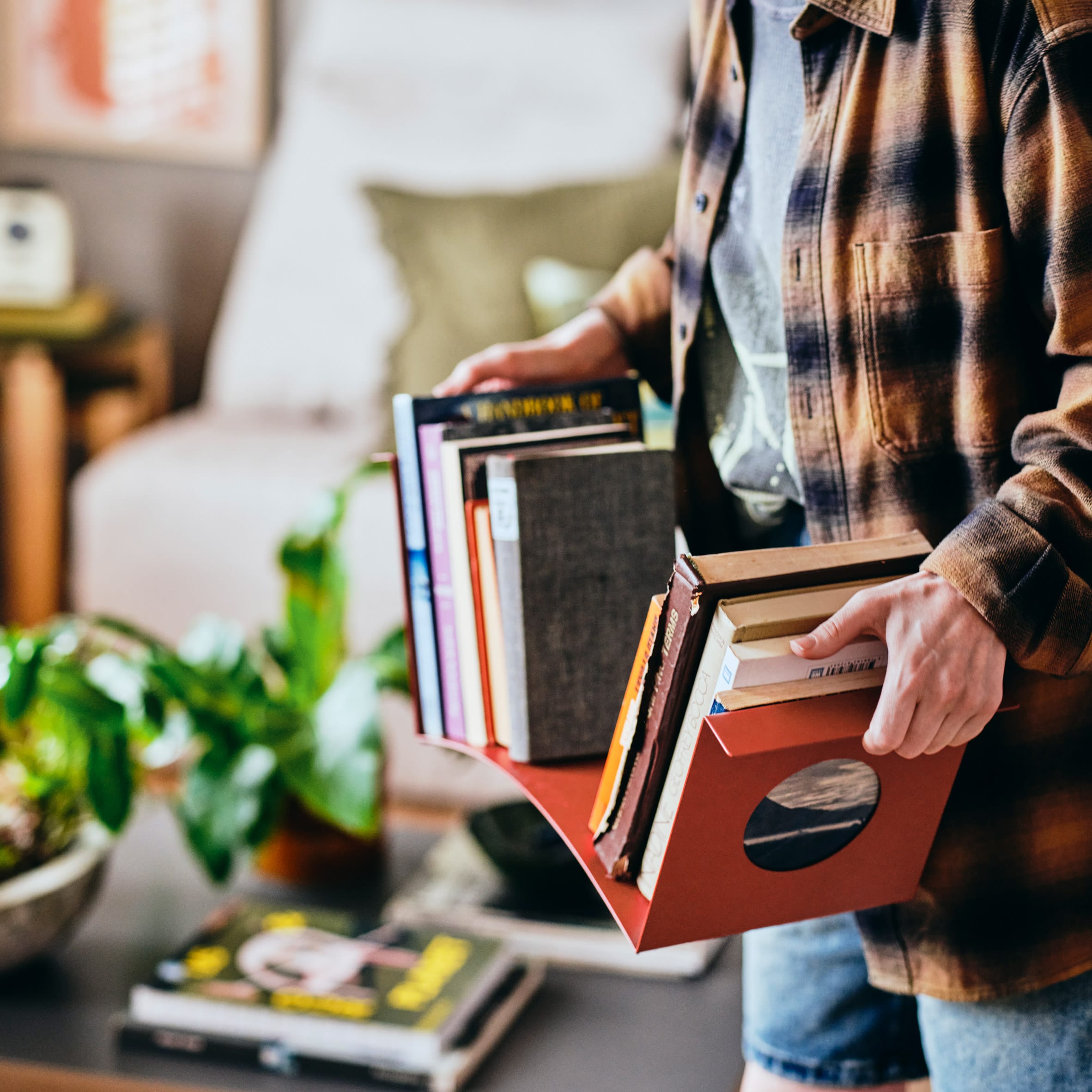 Iemand draagt een stapel boeken in een rode, flexibele organizer met handvatten uit de IKEA KOMPISHÄNG-collectie