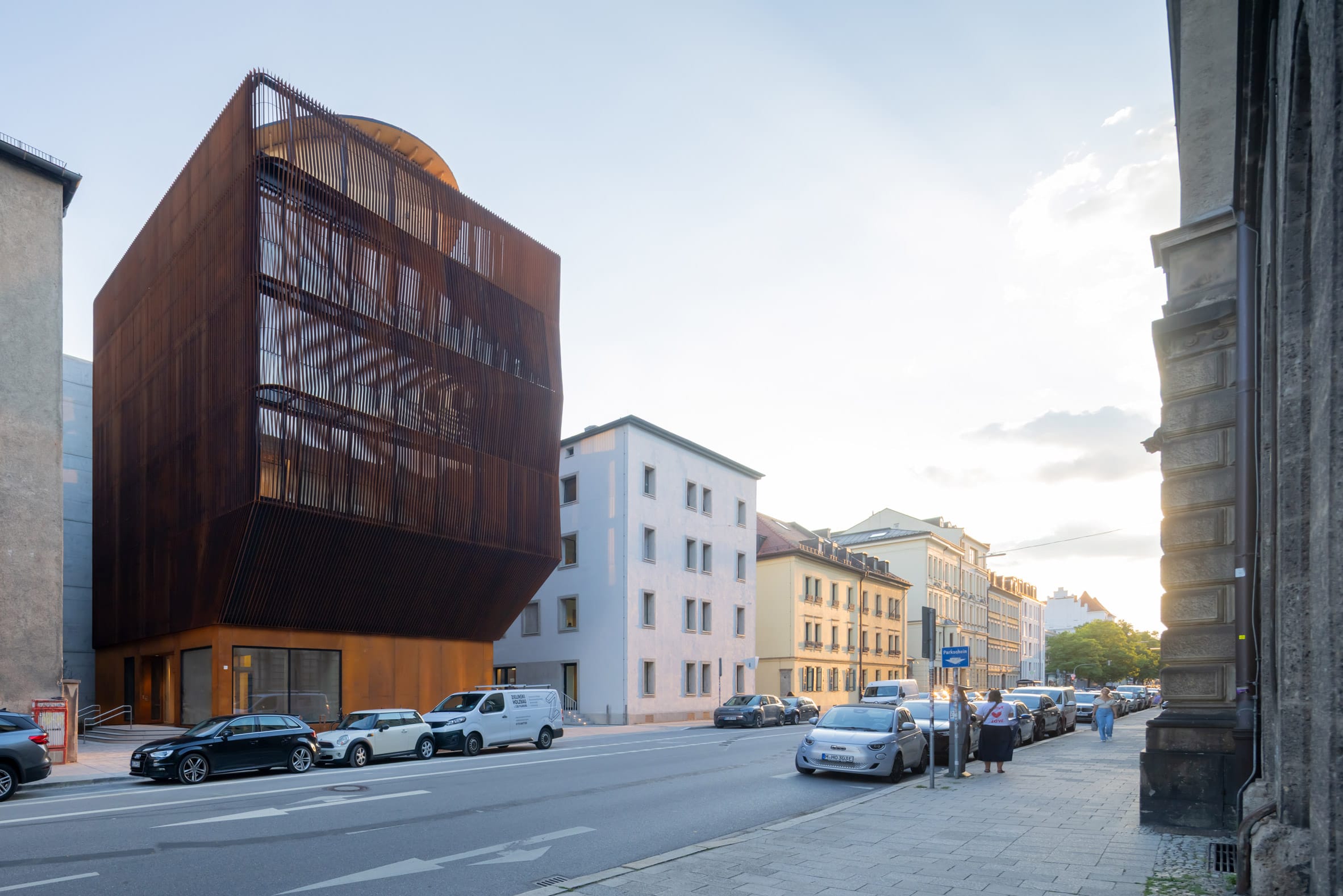 Modern gebouw met een roestbruine gevel van verticale lamellen in een stadsstraat met geparkeerde auto's
