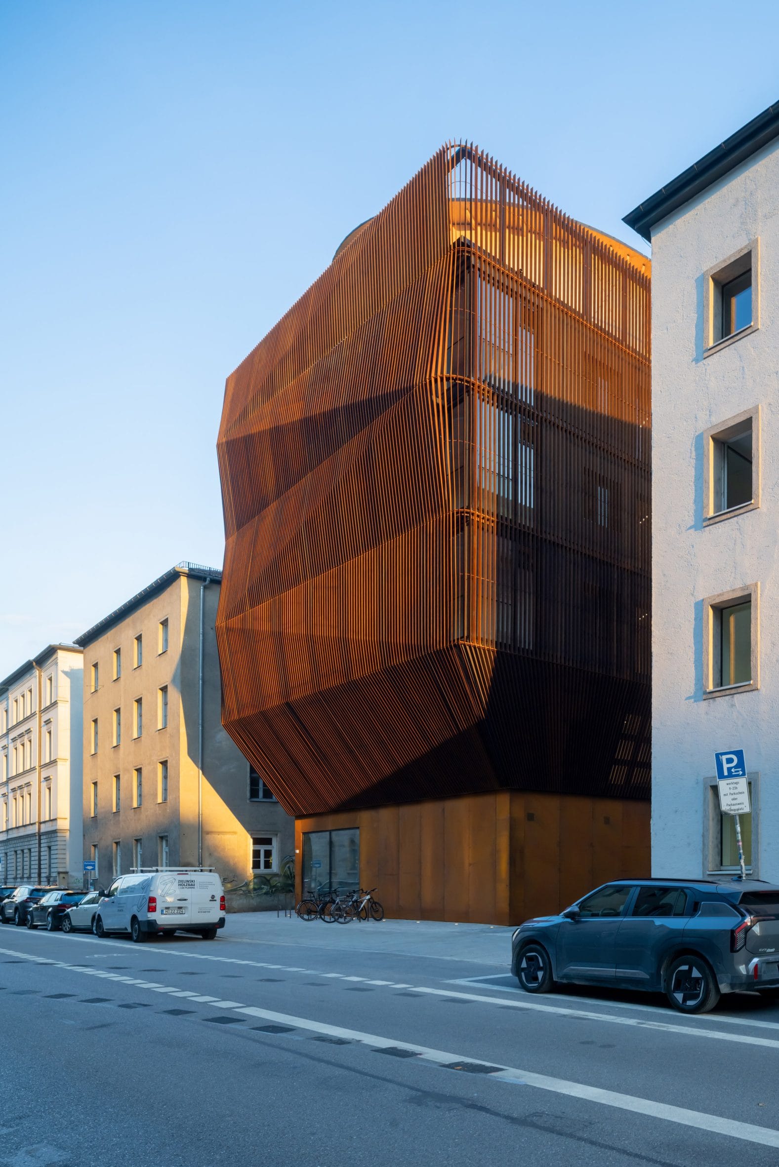 Modern gebouw met een opvallende, hoekige gevel van verticale roestbruine lamellen tussen traditionele stadsarchitectuur