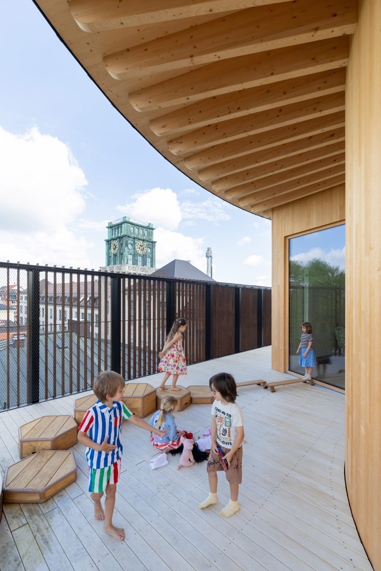 Spelende kinderen op een houten dakterras met uitzicht op een stad met een kerktoren