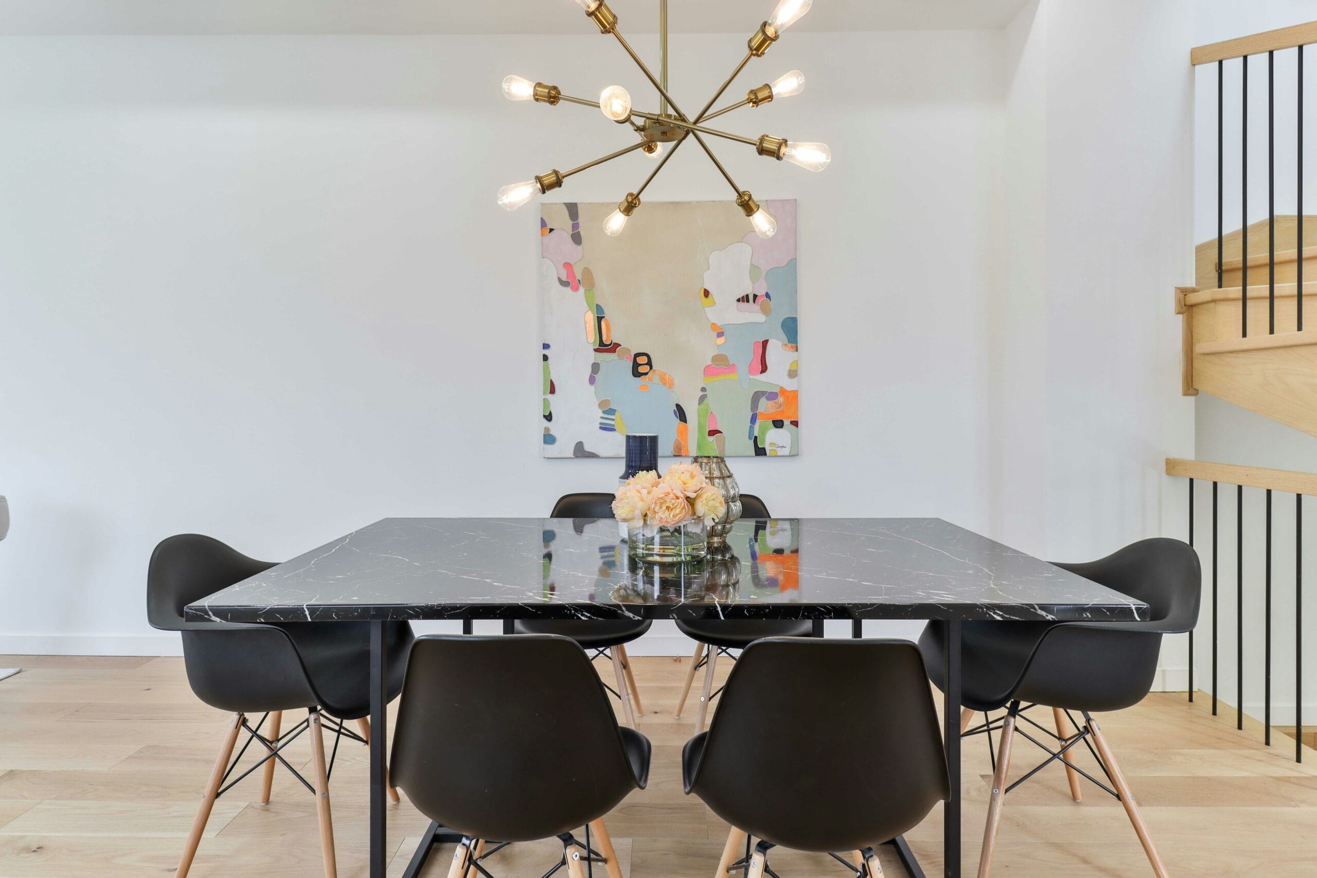 Moderne eetkamer met een zwarte marmeren tafel, zwarte kuipstoelen en een opvallende gouden kroonluchter
