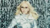 Madonna met blond haar, een zilveren jasje en een bril voor een achtergrond van glinsterende slingers