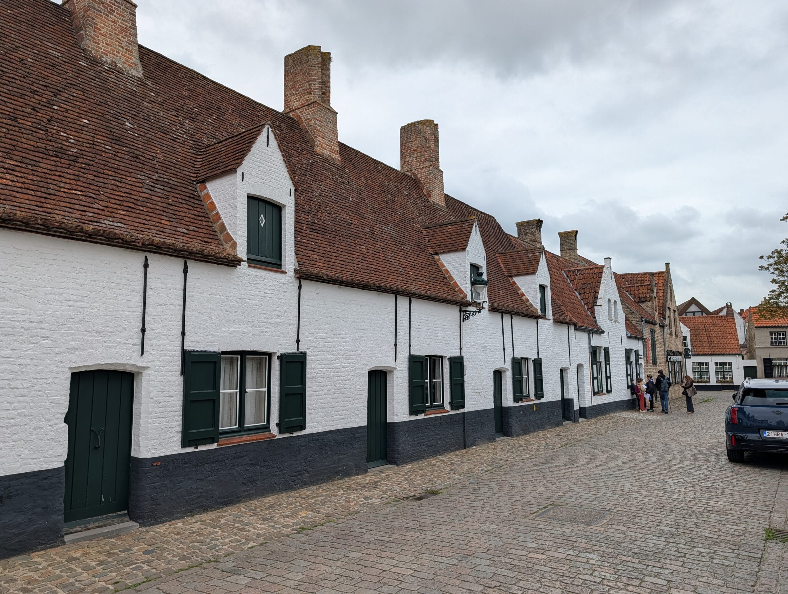 Rij witgekalkte historische huisjes met rode pannendaken en groene luiken aan een kasseistraat in Brugge