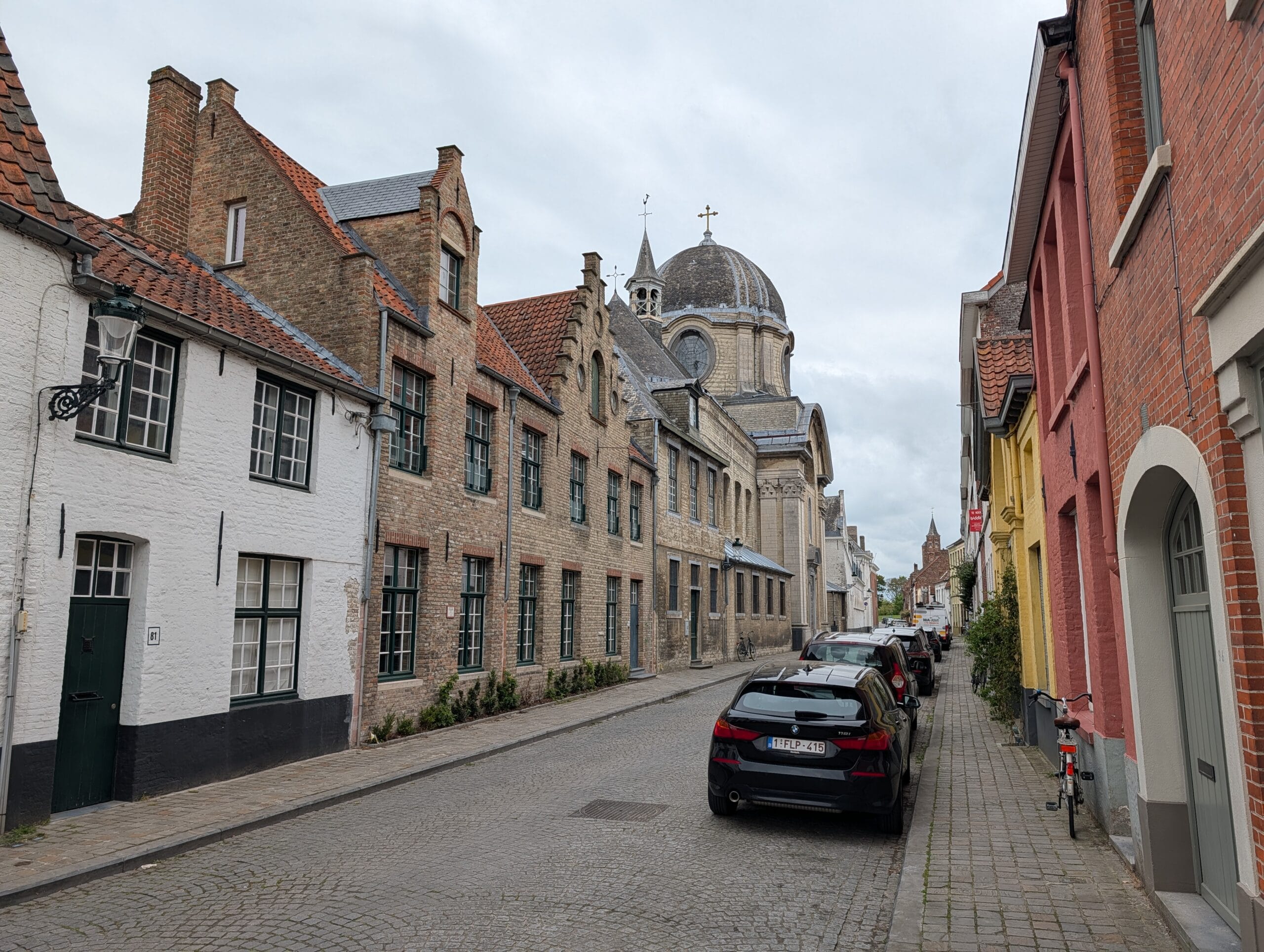 Historische straat in Brugge met kasseien, trapgevels en de koepel van de Engelse Kloosterkerk op de achtergrond