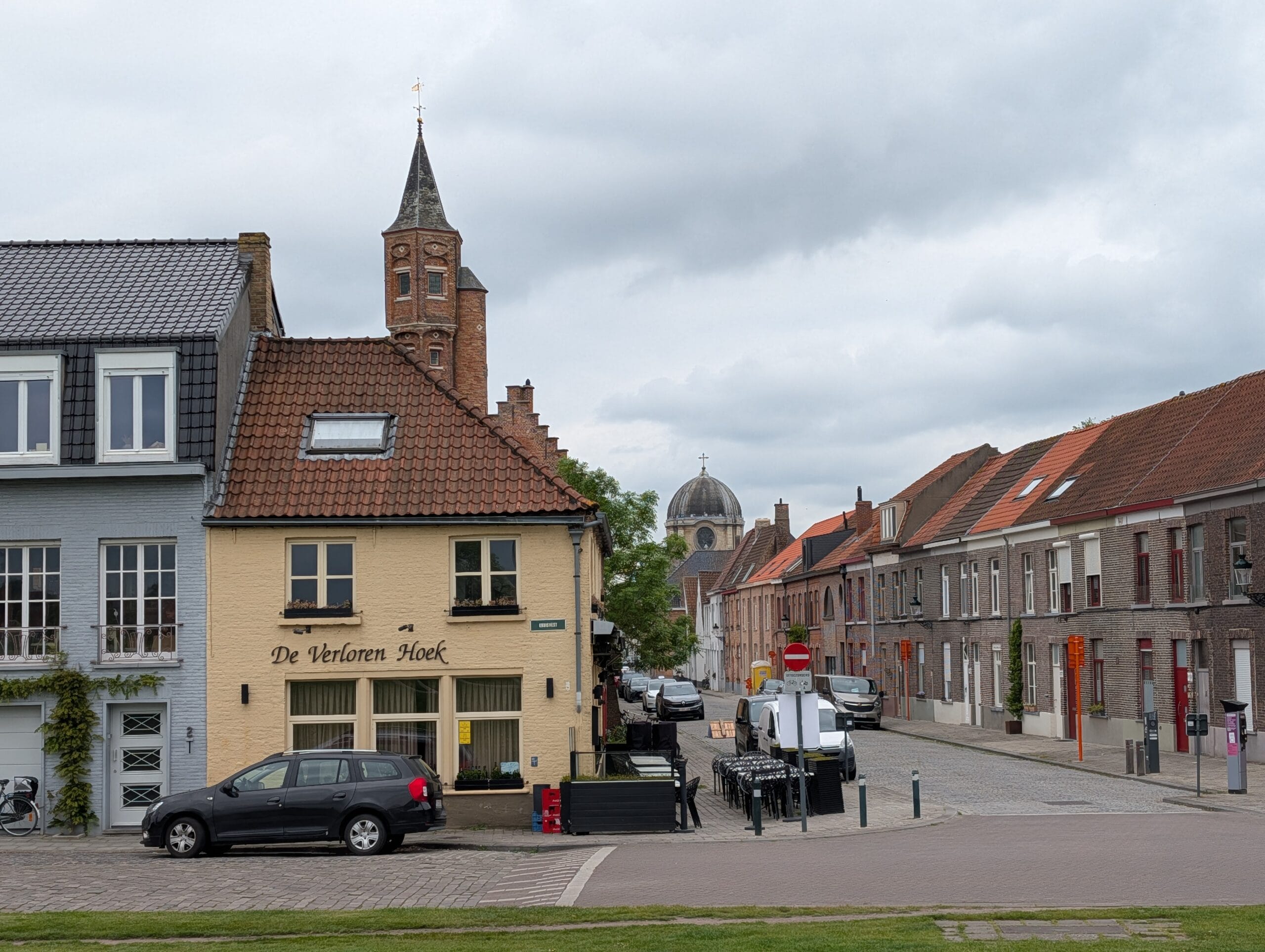Zicht op café De Verloren Hoek in een kasseistraat in Brugge met historische gebouwen en kerktorens op de achtergrond
