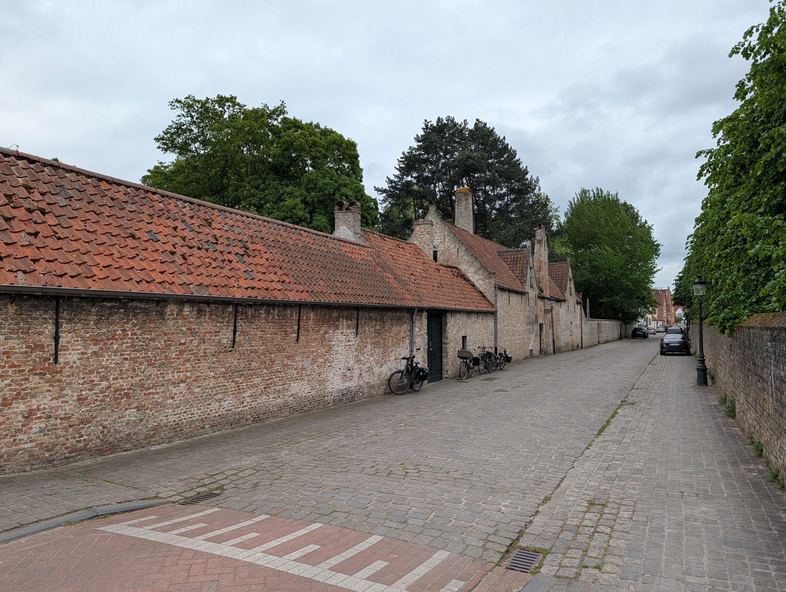 Een rustige straat in Brugge met kasseien en een lange, oude bakstenen muur met rode dakpannen onder een bewolkte lucht