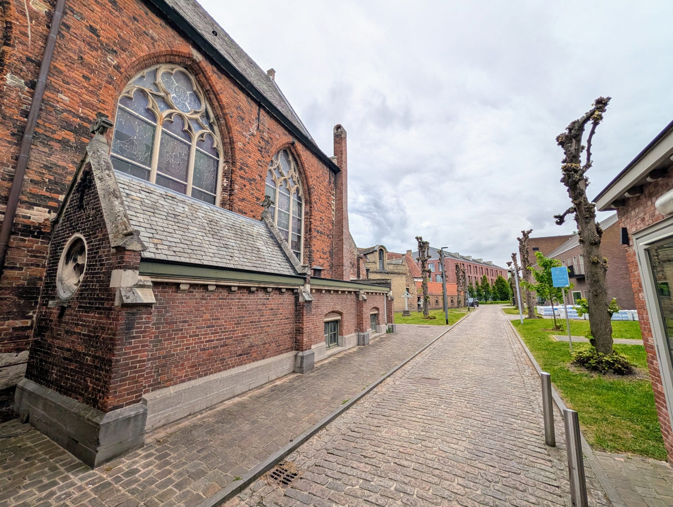 Zicht op een kasseistraat in de wijk Sint-Anna in Brugge, geflankeerd door de bakstenen gevel van een kerk met spitsbogen