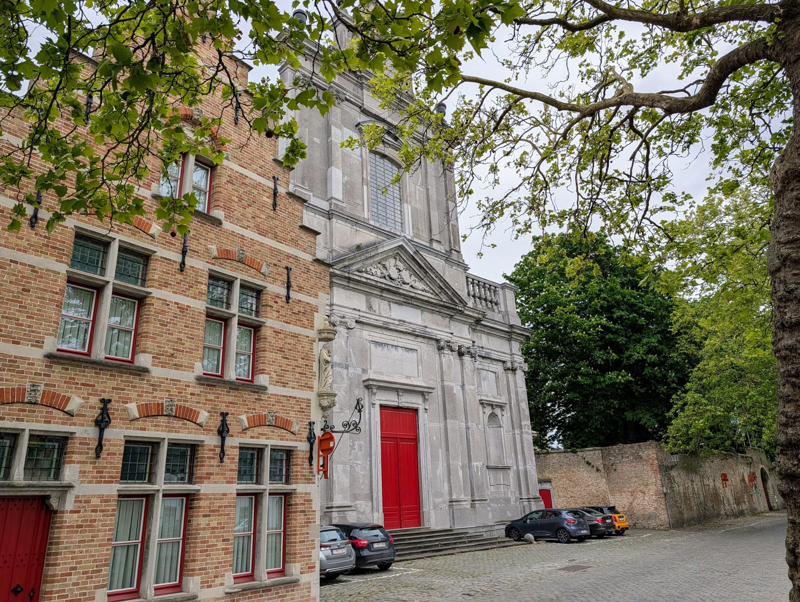 De barokke gevel van de Sint-Walburgakerk in Brugge met een opvallende rode deur, geflankeerd door een bakstenen gebouw