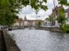 Gezicht op een gracht in Brugge met een stenen boogbrug, historische trapgevels en een kerktoren in de verte