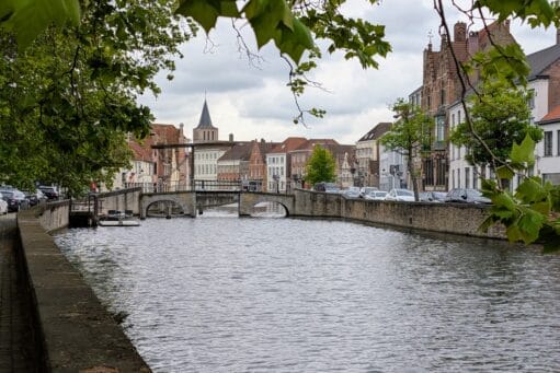 Gezicht op een gracht in Brugge met een stenen boogbrug, historische trapgevels en een kerktoren in de verte
