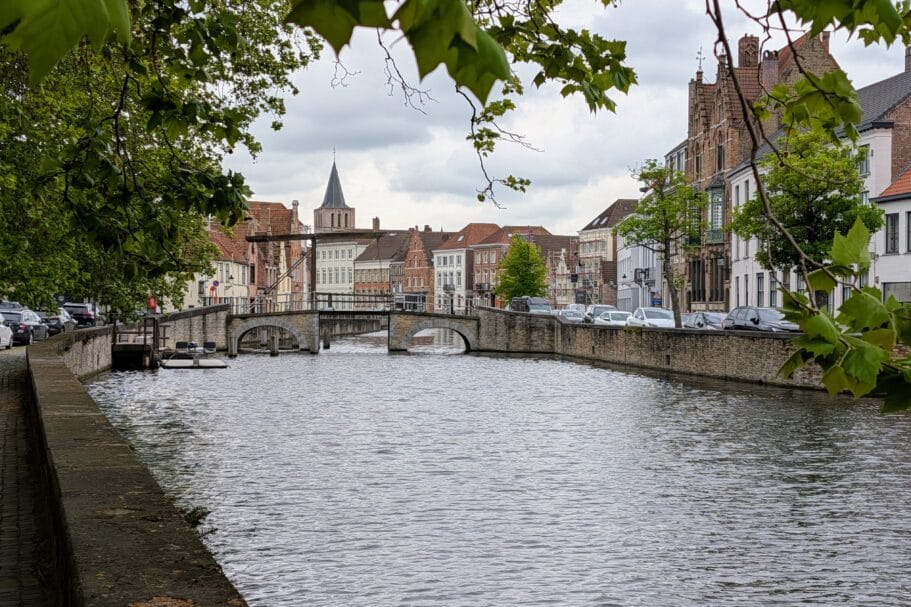 Gezicht op een gracht in Brugge met een stenen boogbrug, historische trapgevels en een kerktoren in de verte