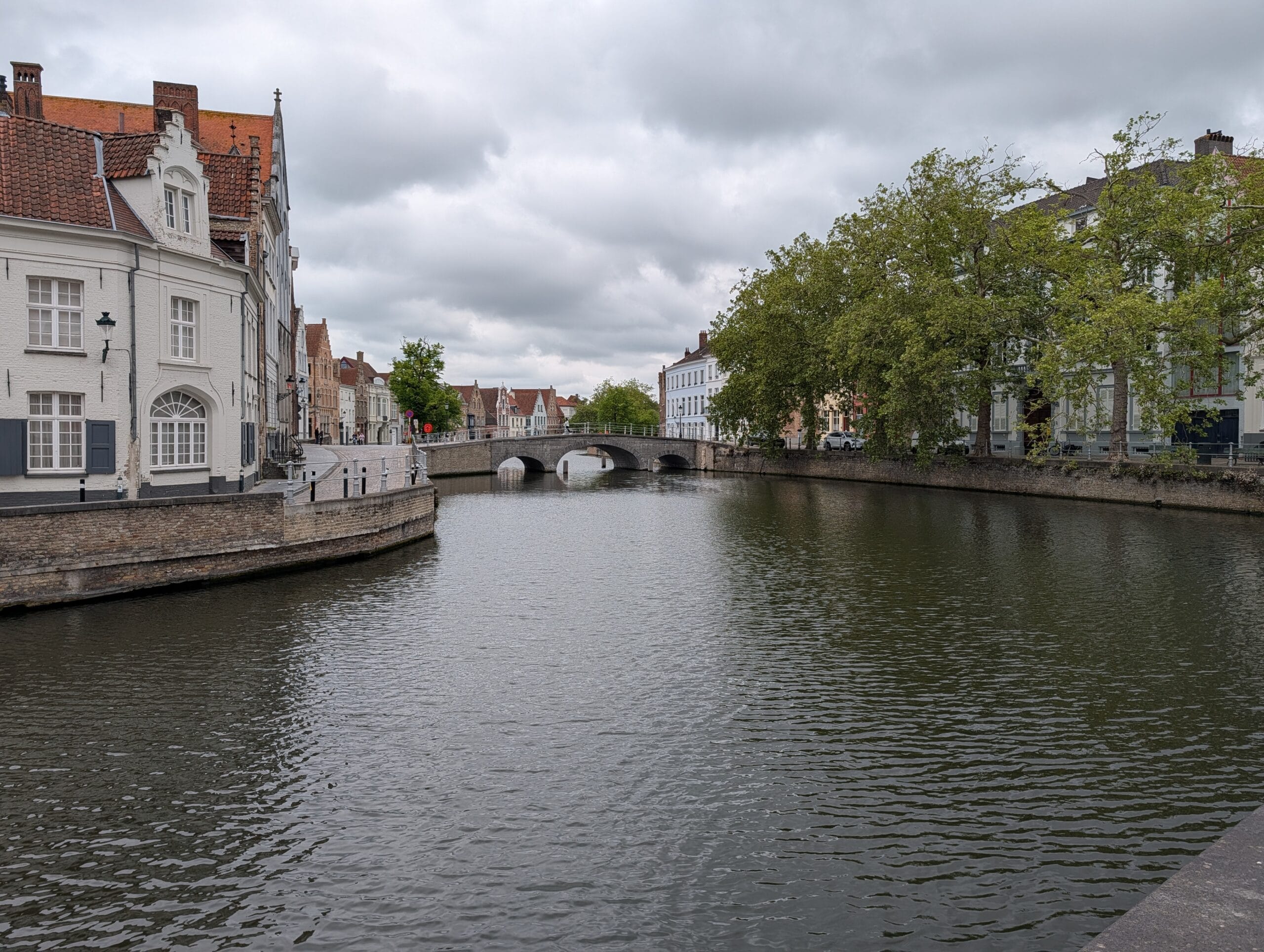 Historische panden langs een kanaal in Brugge met een stenen boogbrug onder een bewolkte hemel