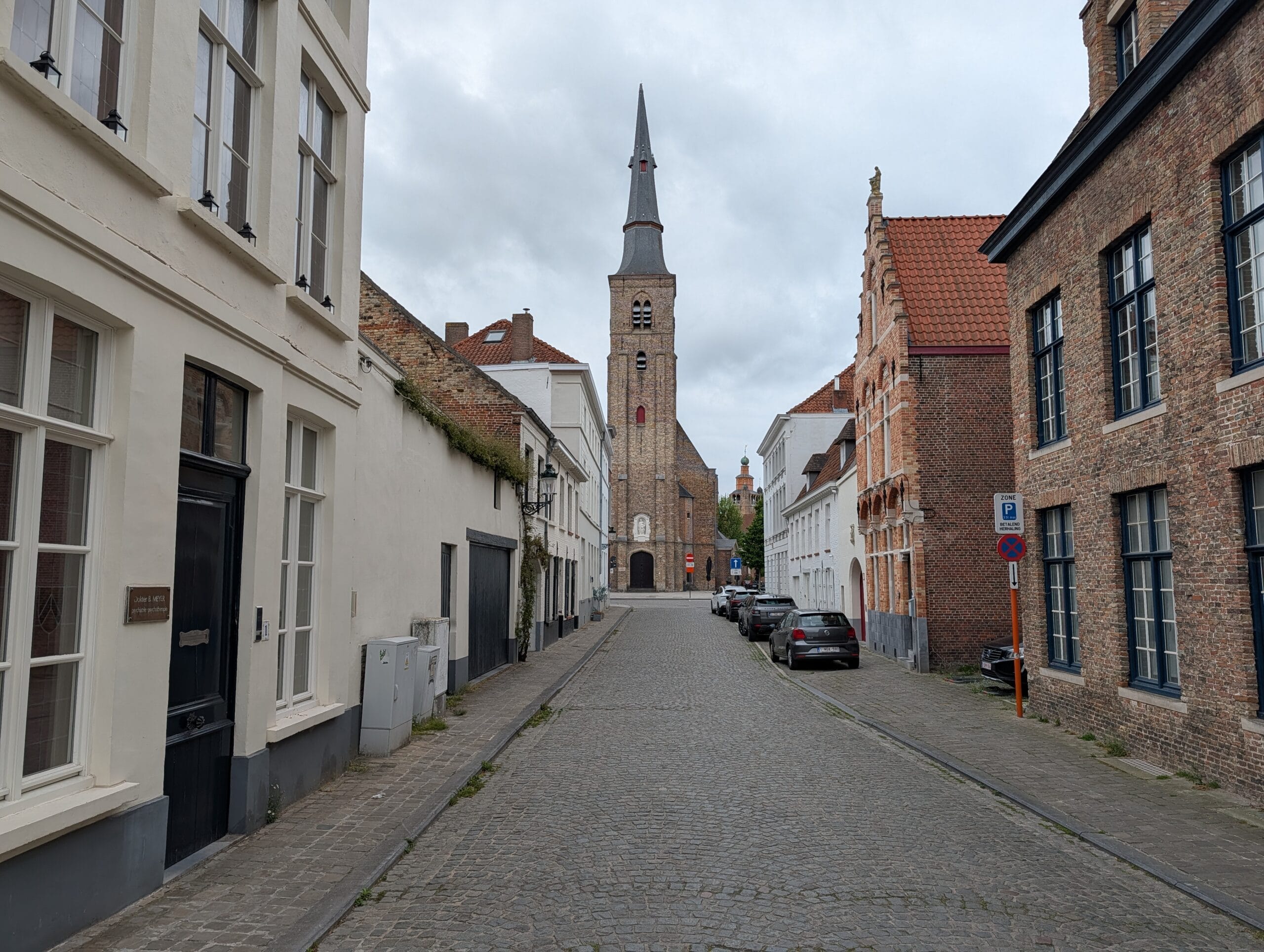 Een smalle kasseistraat in Brugge met historische bakstenen huizen en de Sint-Gilliskerk aan het einde van de weg