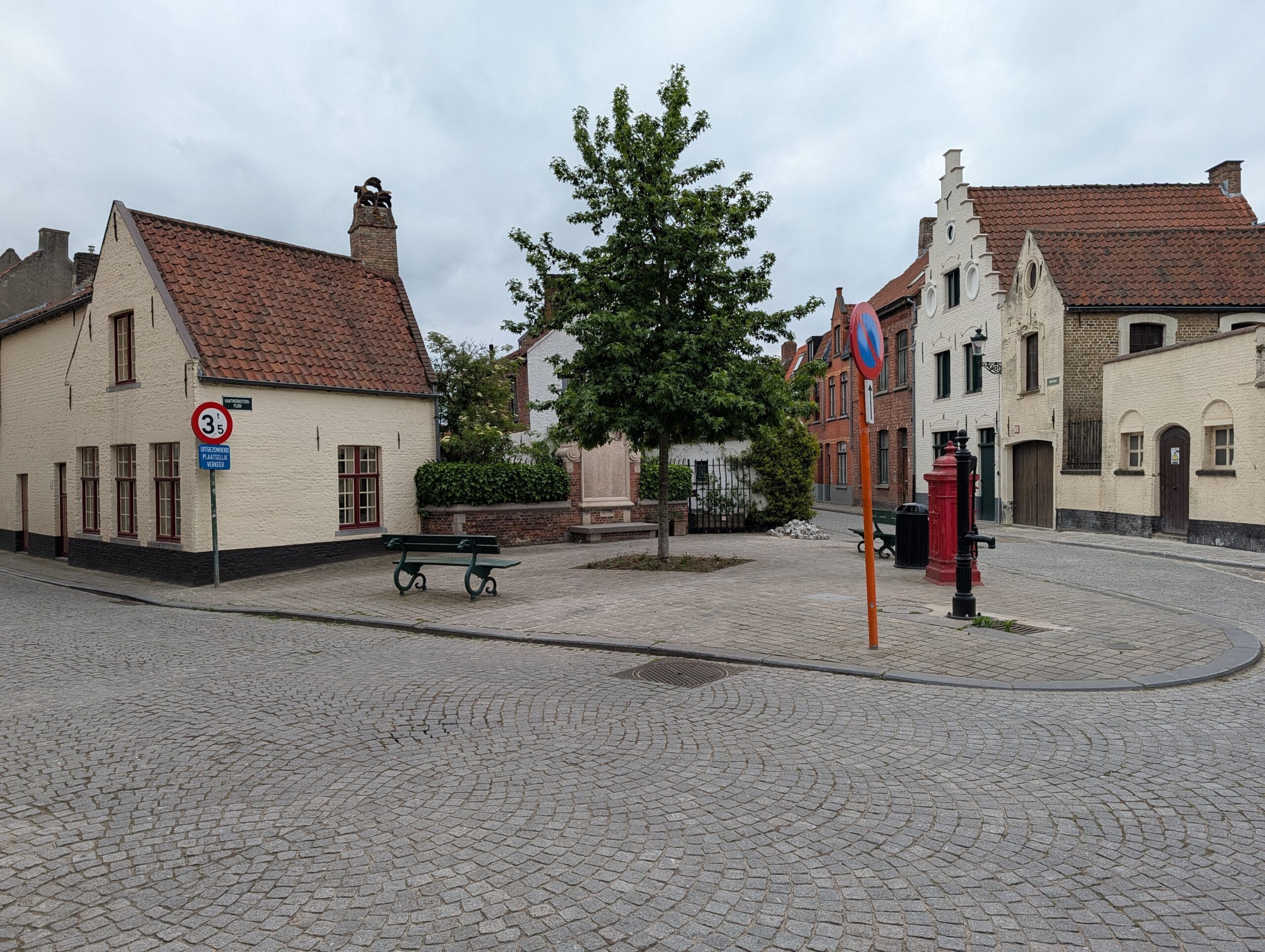 Historisch plein met kasseien, witgekalkte trapgevelwoningen, een centrale boom en een rode waterpomp in Brugge