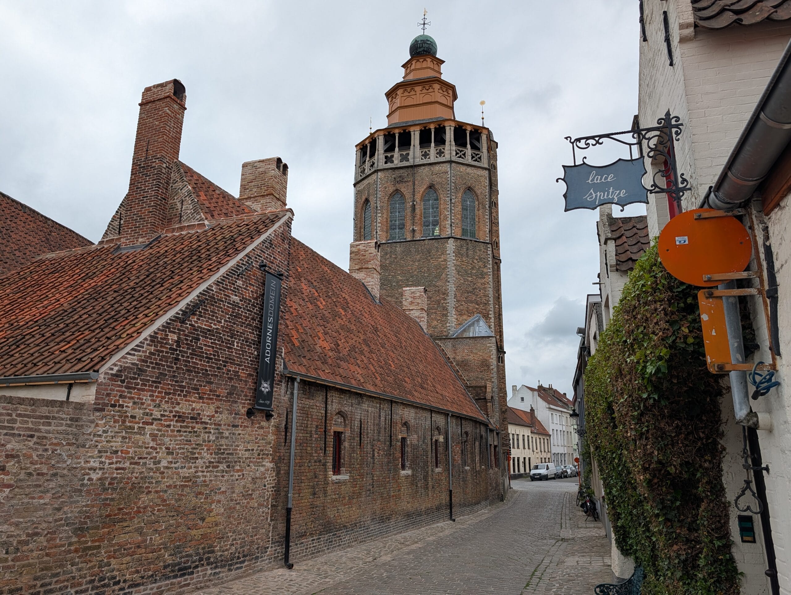 De Jeruzalemkerk en het Adornesdomein in een smalle kasseistraat in Brugge onder een bewolkte hemel