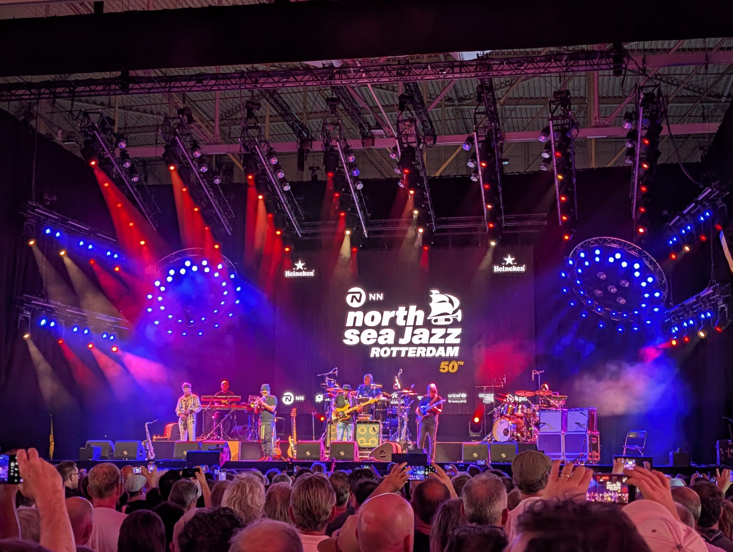 Marcus Miller en zijn band treden op in een grote zaal op North Sea Jazz onder felle rode en blauwe lichten