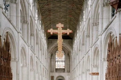 Interieur van een kathedraal met een groot hangend kruis boven het gangpad en een beschilderd houten plafond